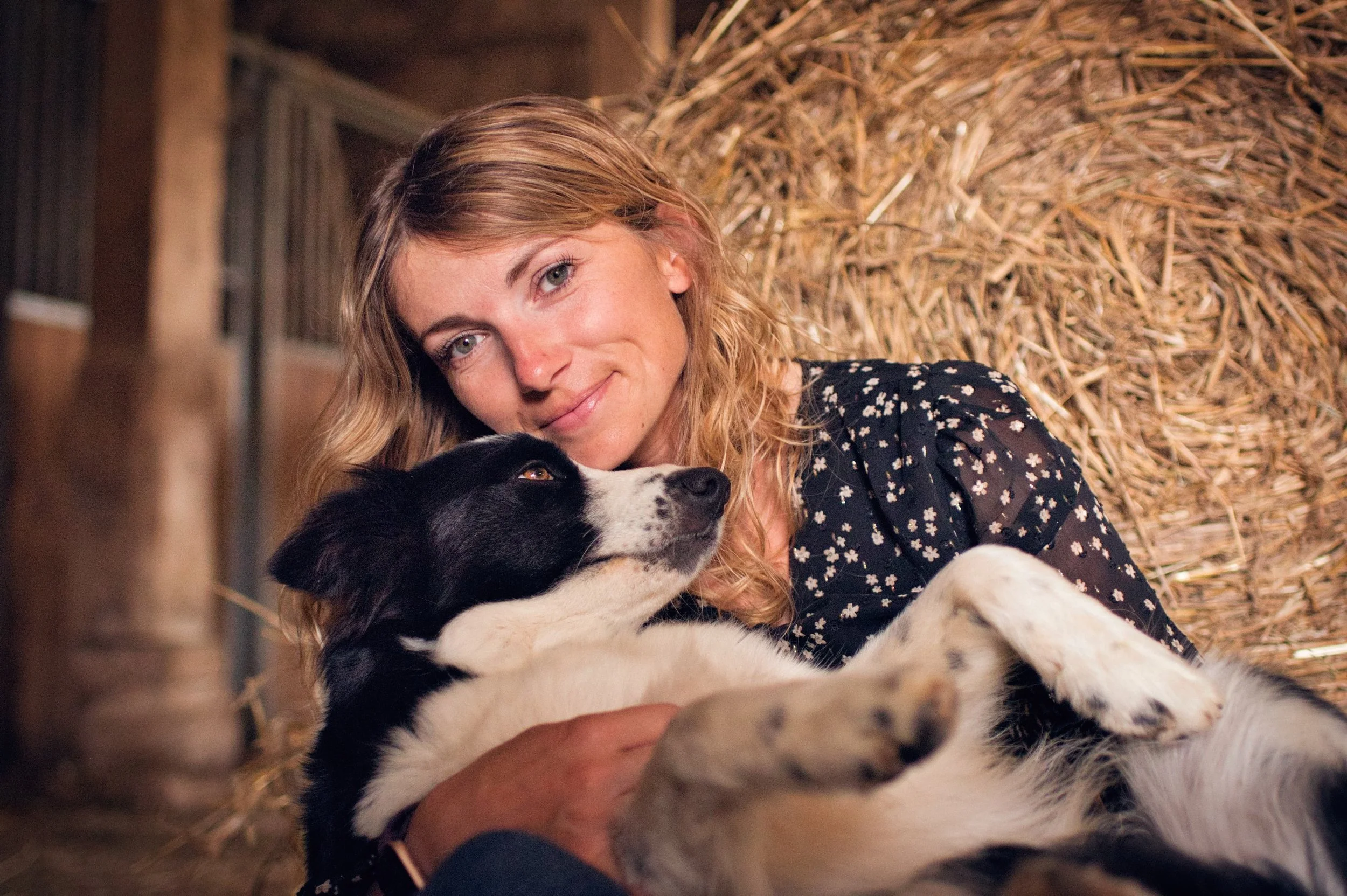 portrait d'une femme avec sa border coli, dans une grange sur une balle de paille