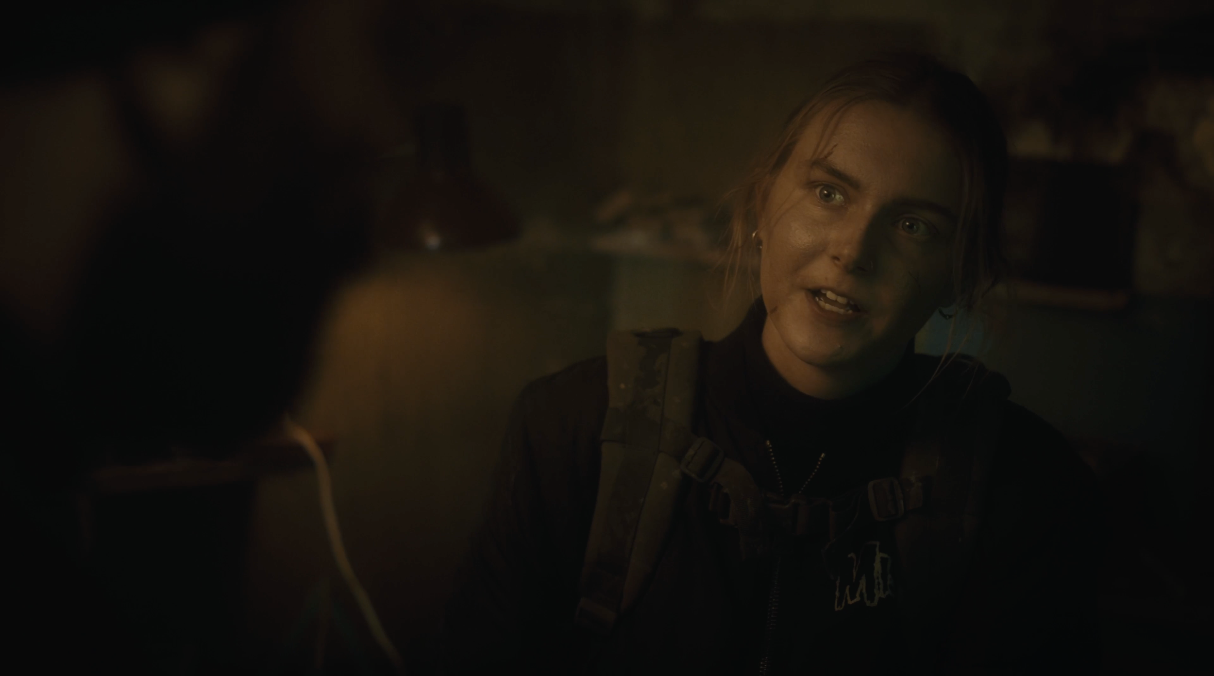 Eine junge Frau mit nassen Haaren und Rucksack spricht in einem dunklen Raum.