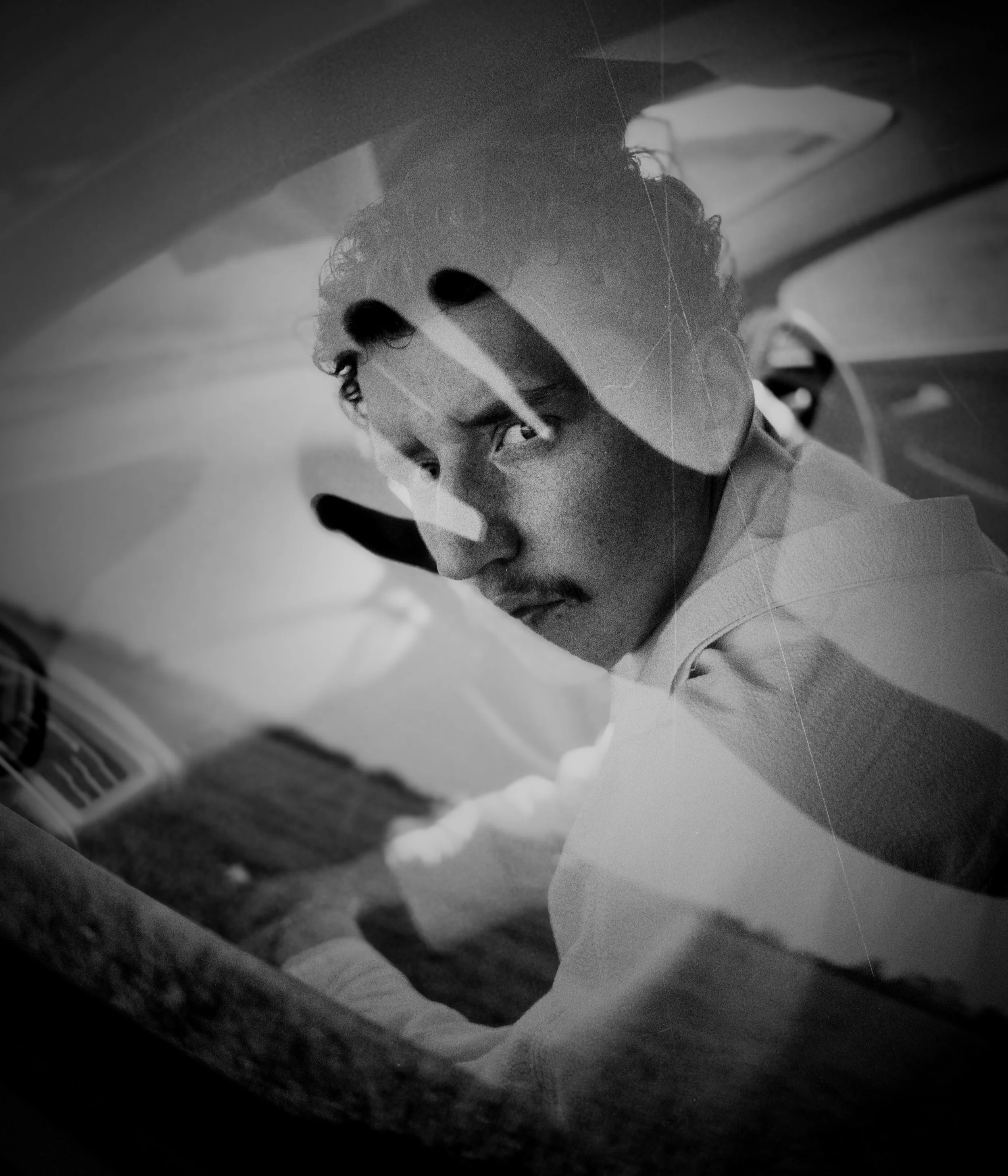 Schwarz-Weiß-Foto eines Mannes, der in einem Auto sitzt und durch die Windschutzscheibe schaut.