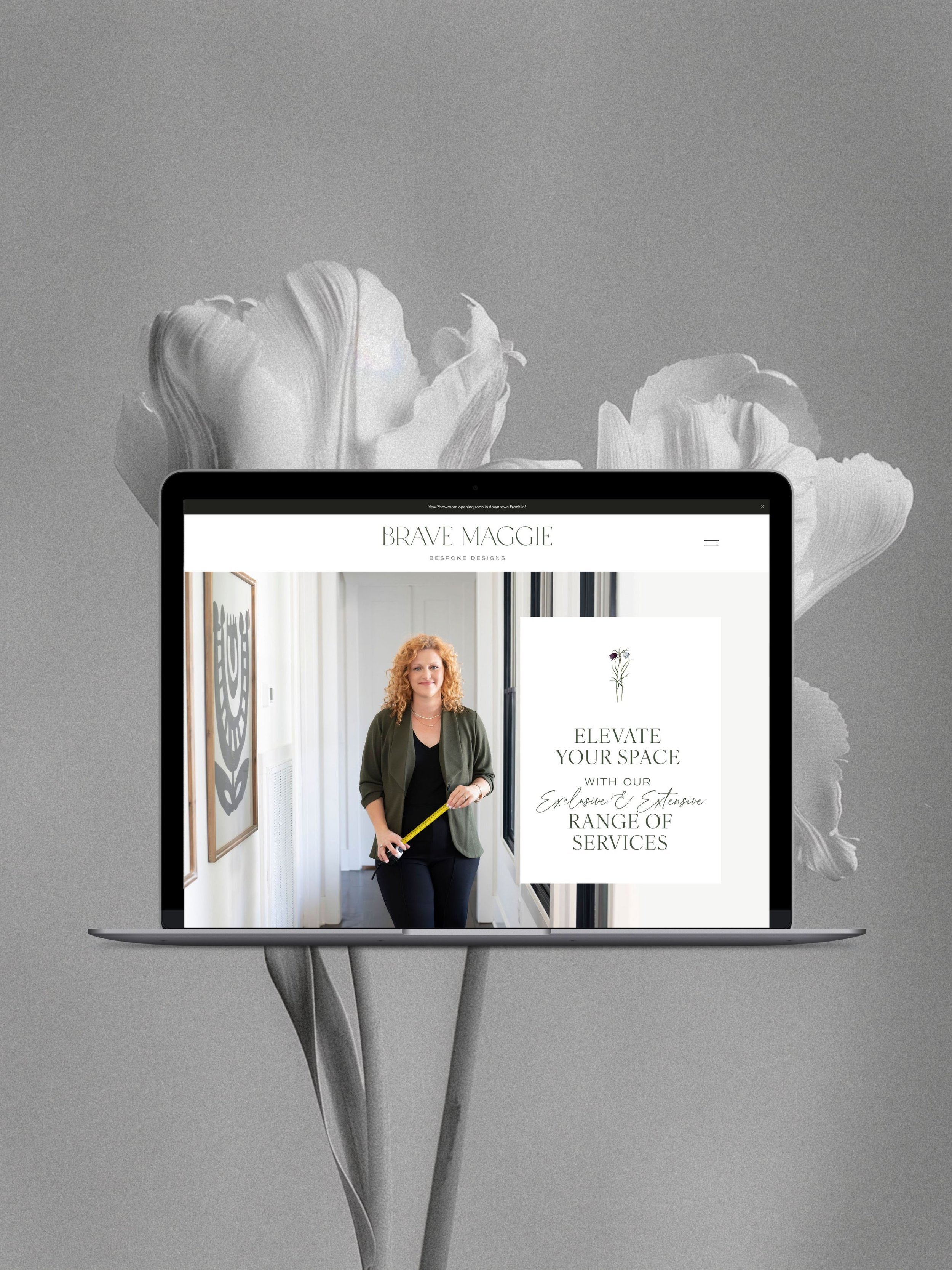 A laptop computer displaying a website for "Brave Maggie" interior design services, with a woman holding a measuring tape standing in a modern, well-lit interior space.