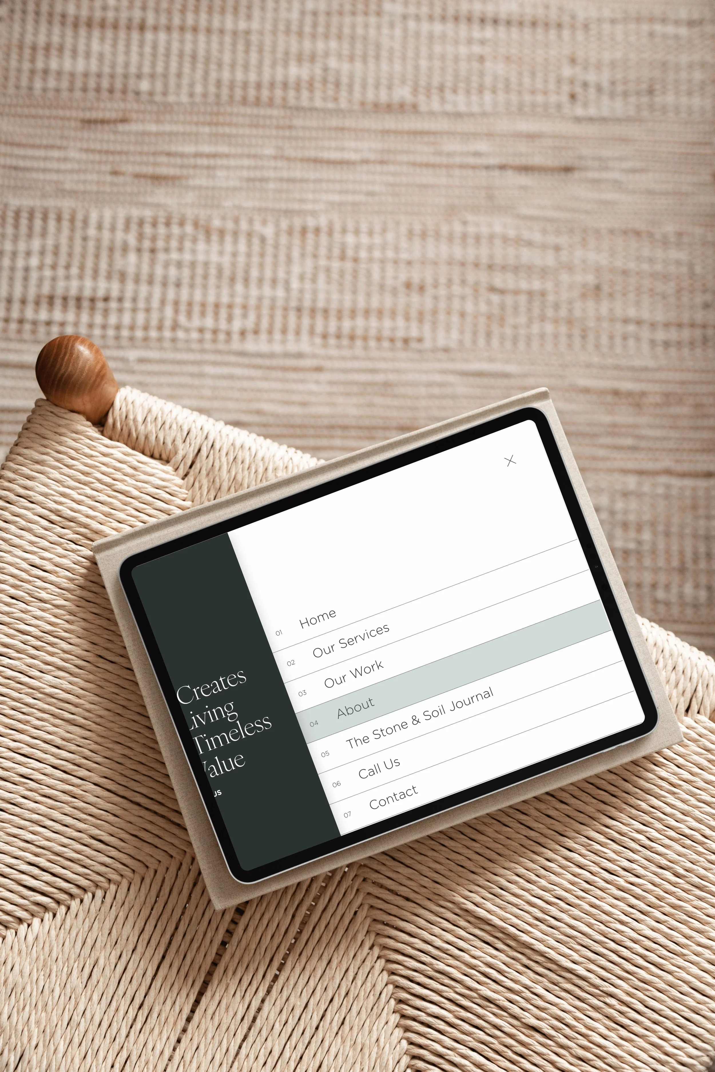 Close-up of a tablet displaying a website menu on a woven rattan surface, with a wooden-handled woven basket partially visible.