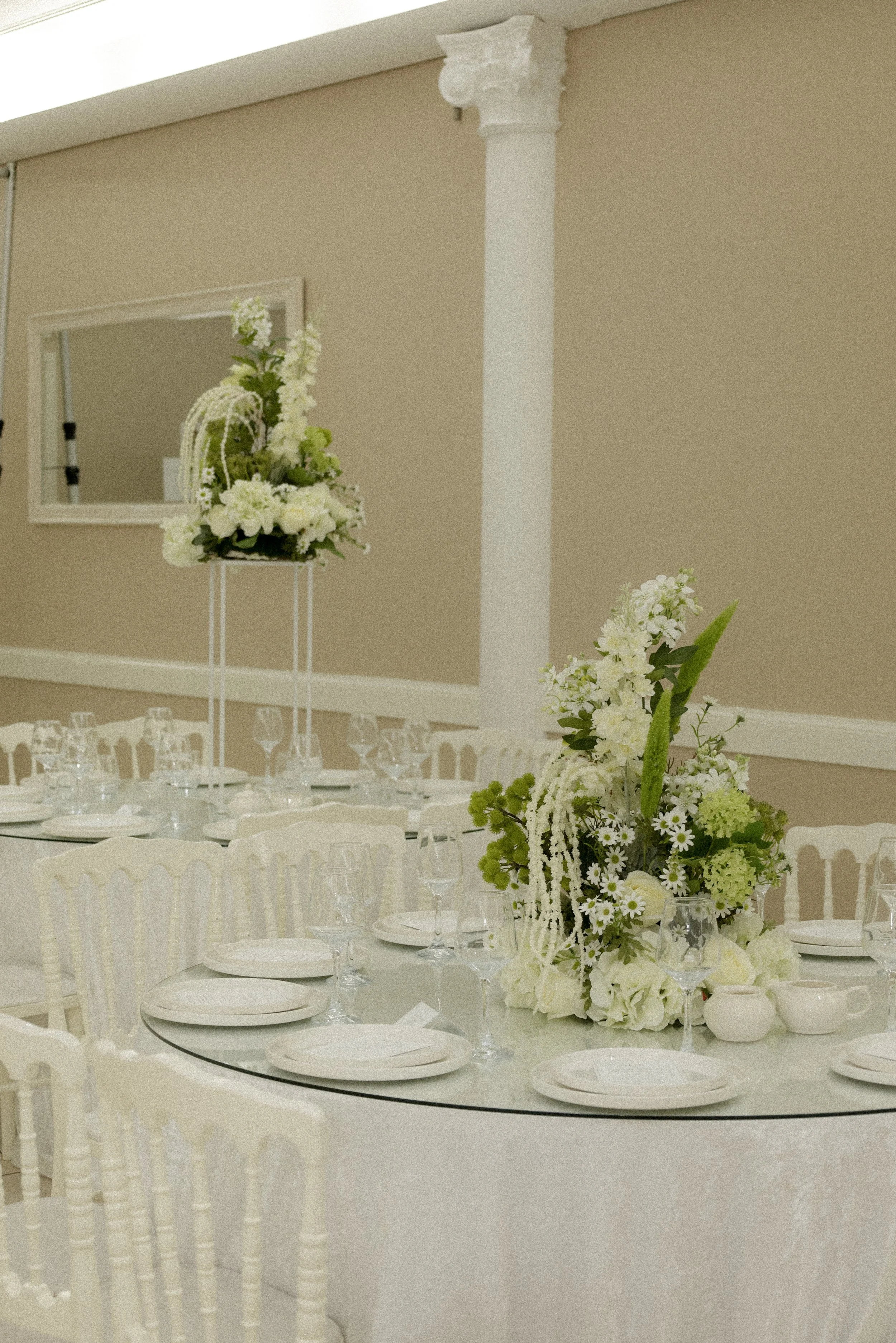 Elegante feesttafel met witte borden, glazen en zilveren bestek, versierd met een bloemstuk met witte en groene bloemen.