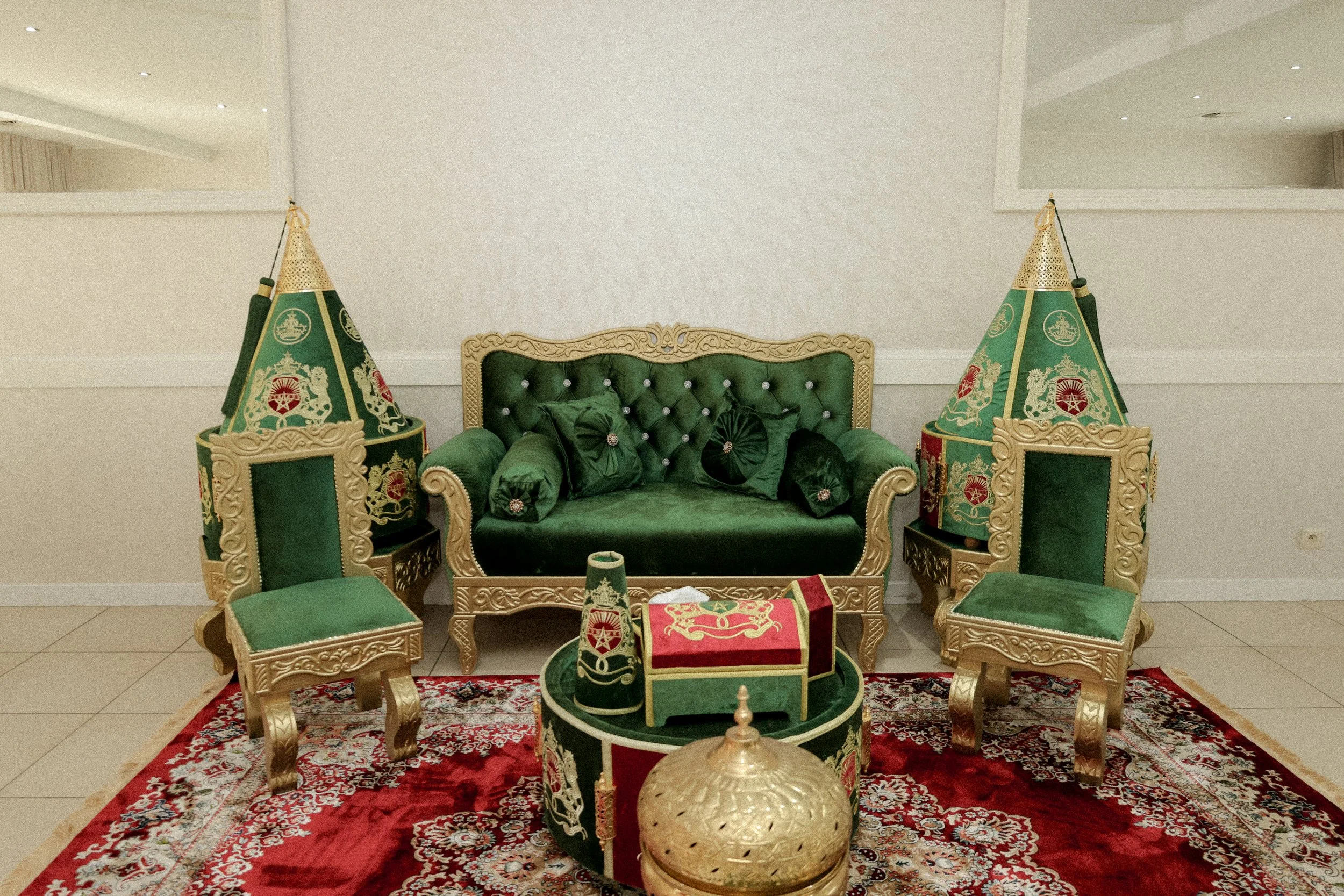 Groene en gouden traditionele Iraanse zitbank en stoelen met kussens, decoratief tapijt, en piramiden-vormige tenten with medailles, all in een salon.