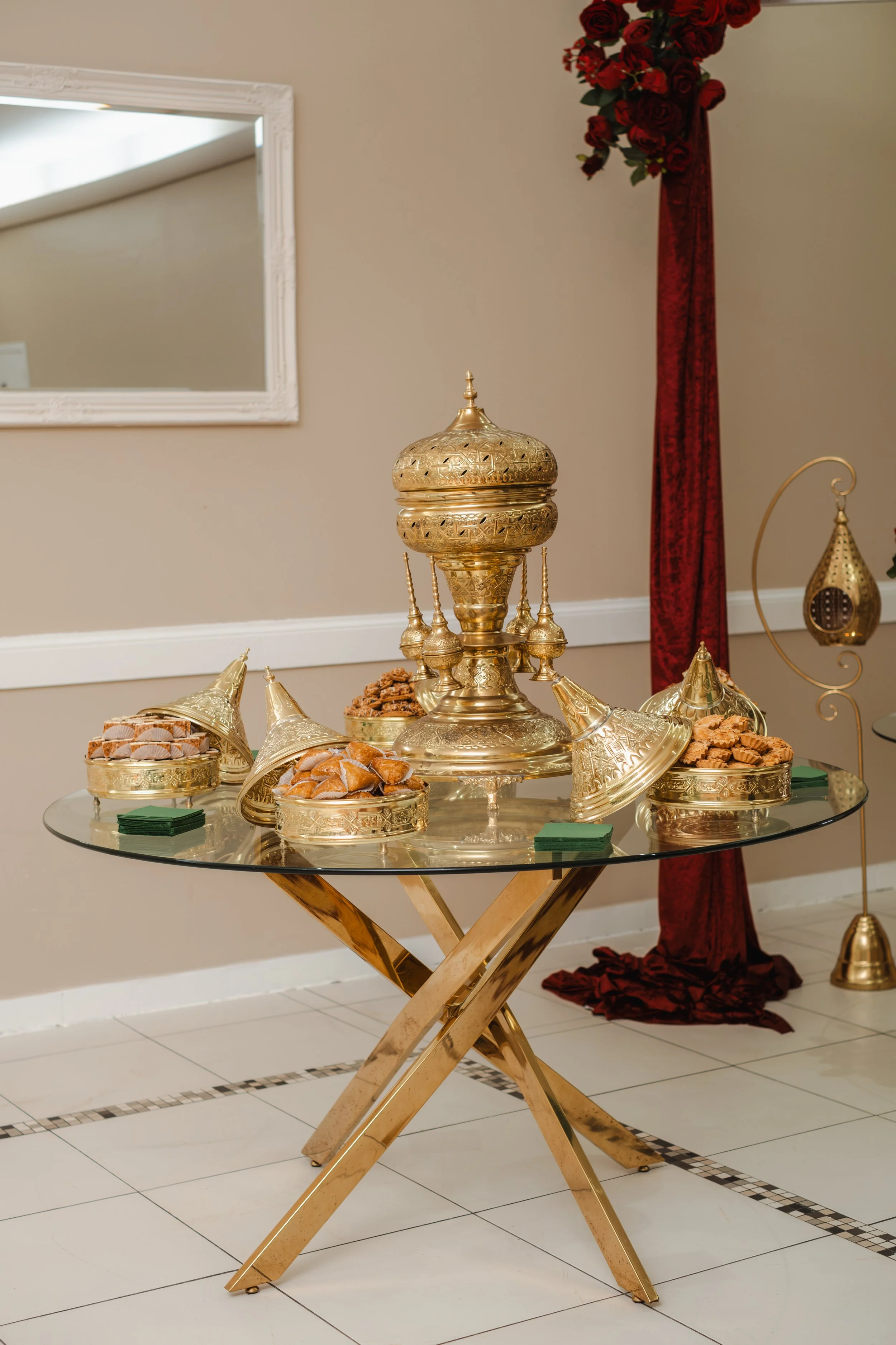 Goudkleurige decoratieve schalen en ornamenten op een glazen tafel, met snoep en snacks, in een elegante interieurruimte.