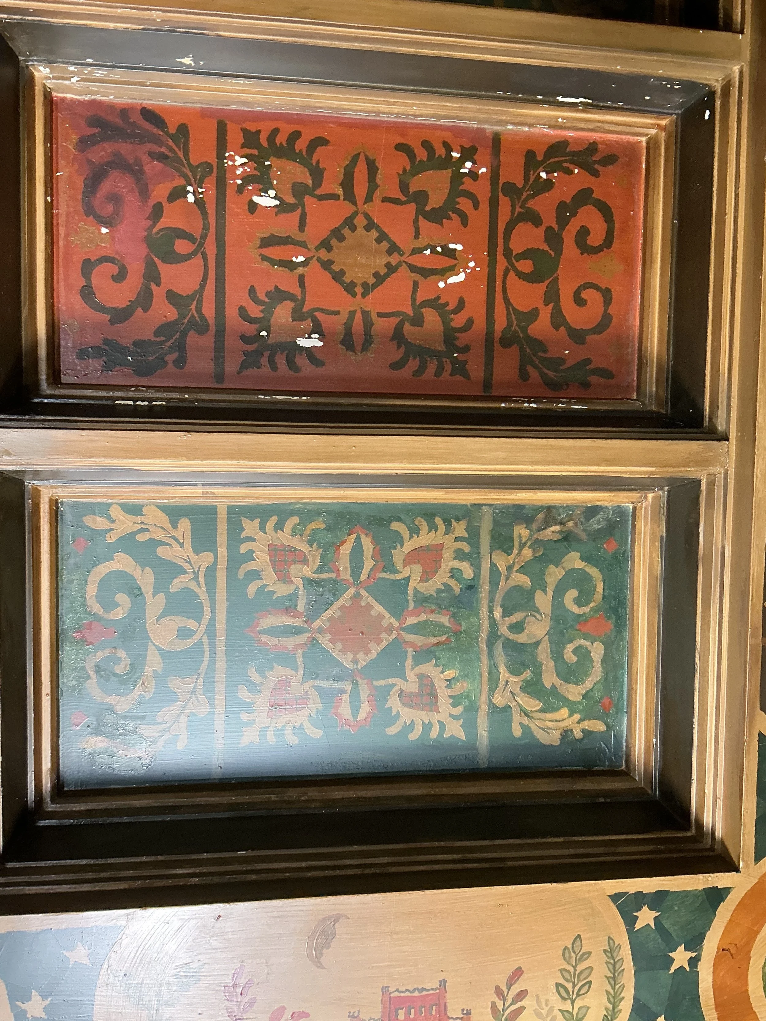 Decorative wooden frame with painted floral and geometric design, predominantly red, green, and gold colors.