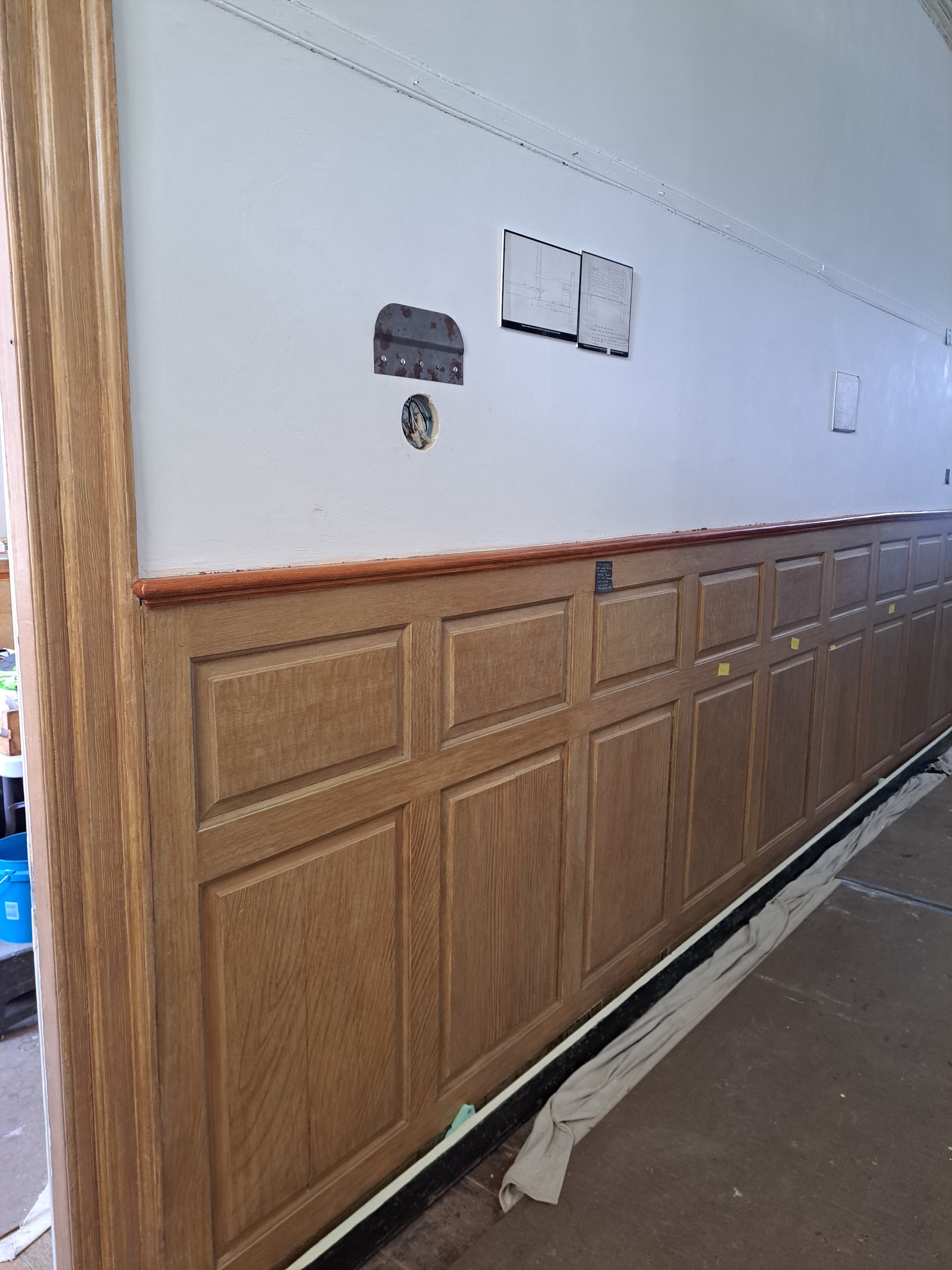 Interior of a house with wood-paneled lower walls, white upper walls, a hole with electrical wiring, and a partially missing or covered thermostat.