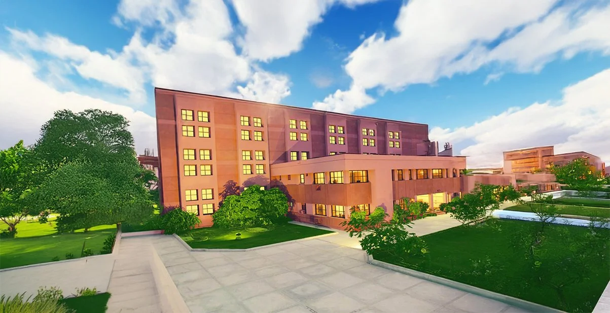 Modern multi-story building with large windows, surrounded by green trees and landscaped lawn, under a partly cloudy blue sky.