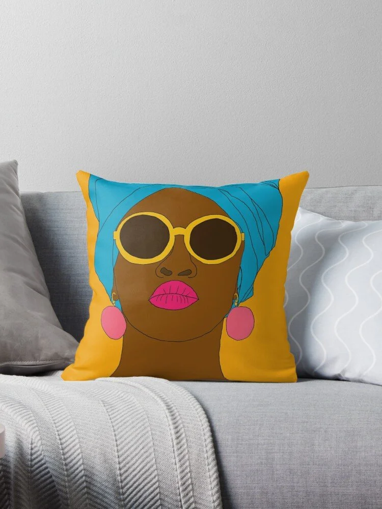 Decorative pillow on a sofa featuring a stylized portrait of a woman with dark skin, wearing yellow sunglasses, a blue headscarf, pink earrings, and pink lipstick.