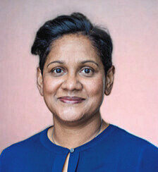 A portrait of a woman with short dark hair wearing a blue top, smiling gently, against a pink background.