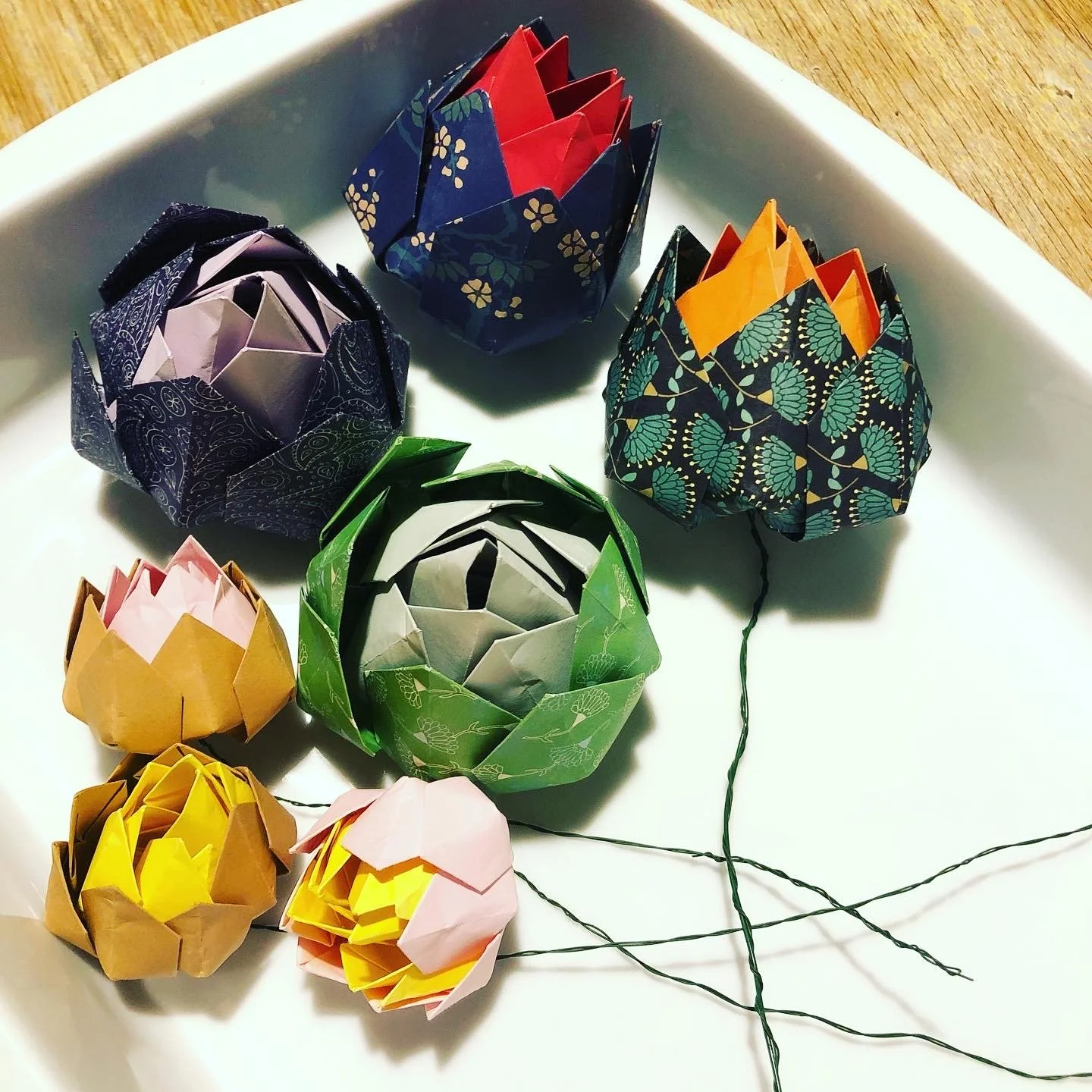 Colored origami paper flowers arranged on a white plate.