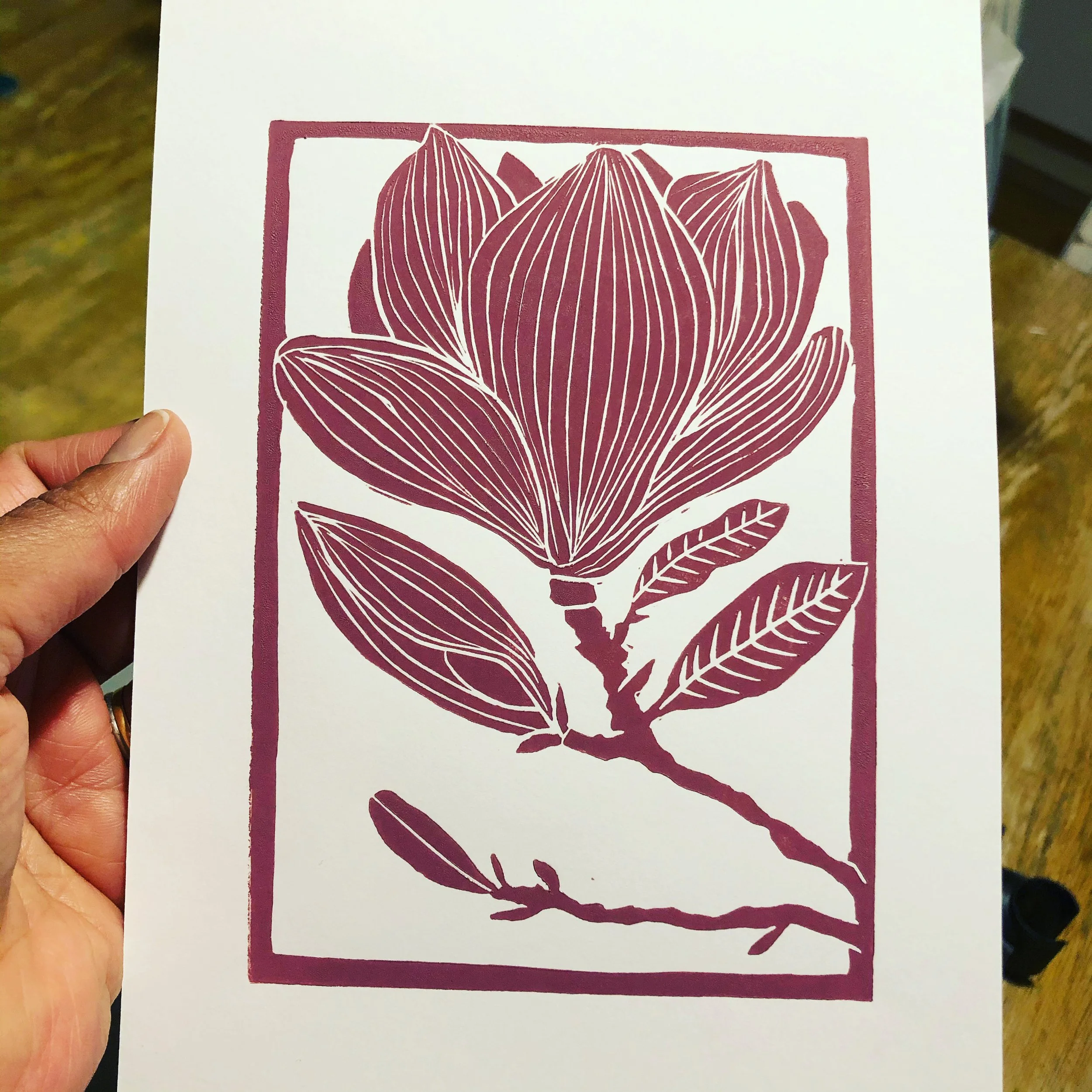 A white paper with a maroon-colored illustration of a magnolia flower and leaves, enclosed in a rectangular border.