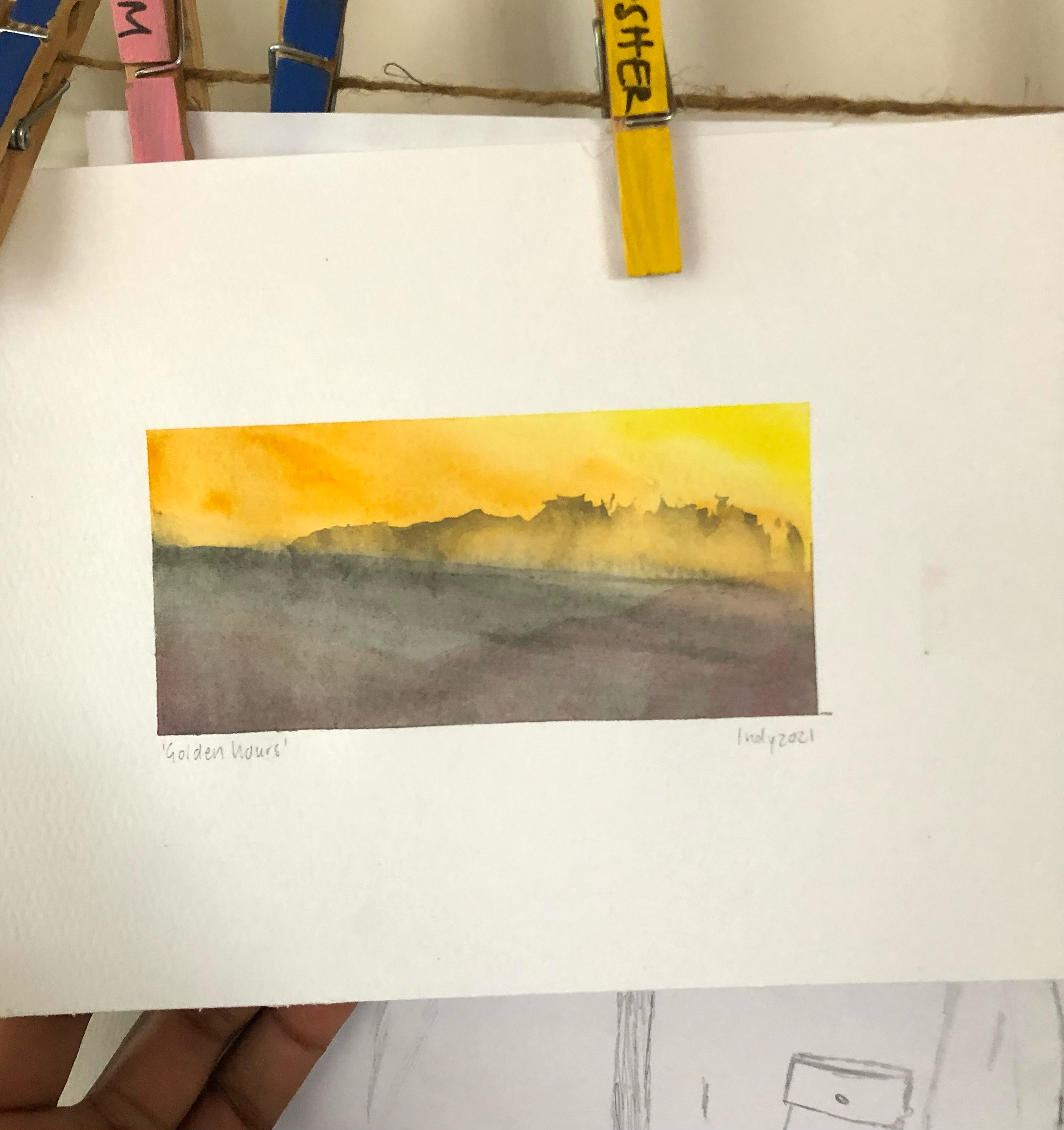 Watercolor painting of a sunset with yellow and orange sky over dark horizon and landscape, titled 'Golden Hours'.