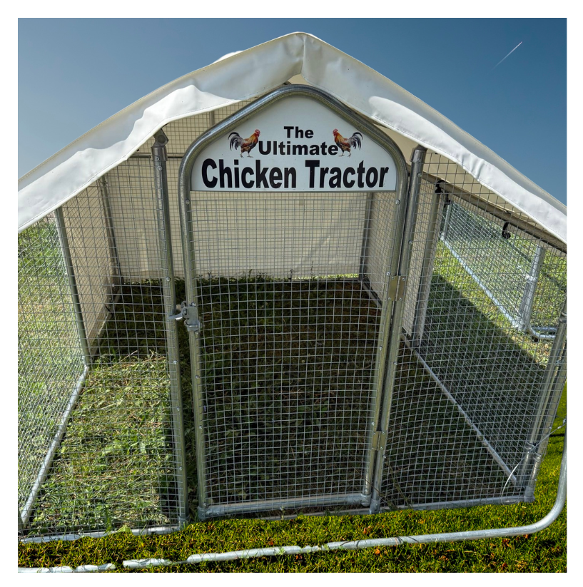 A metal chicken tractor cage with a white canopy, labeled 'The Ultimate Chicken Tractor,' sitting on grass with a bright blue sky in the background.