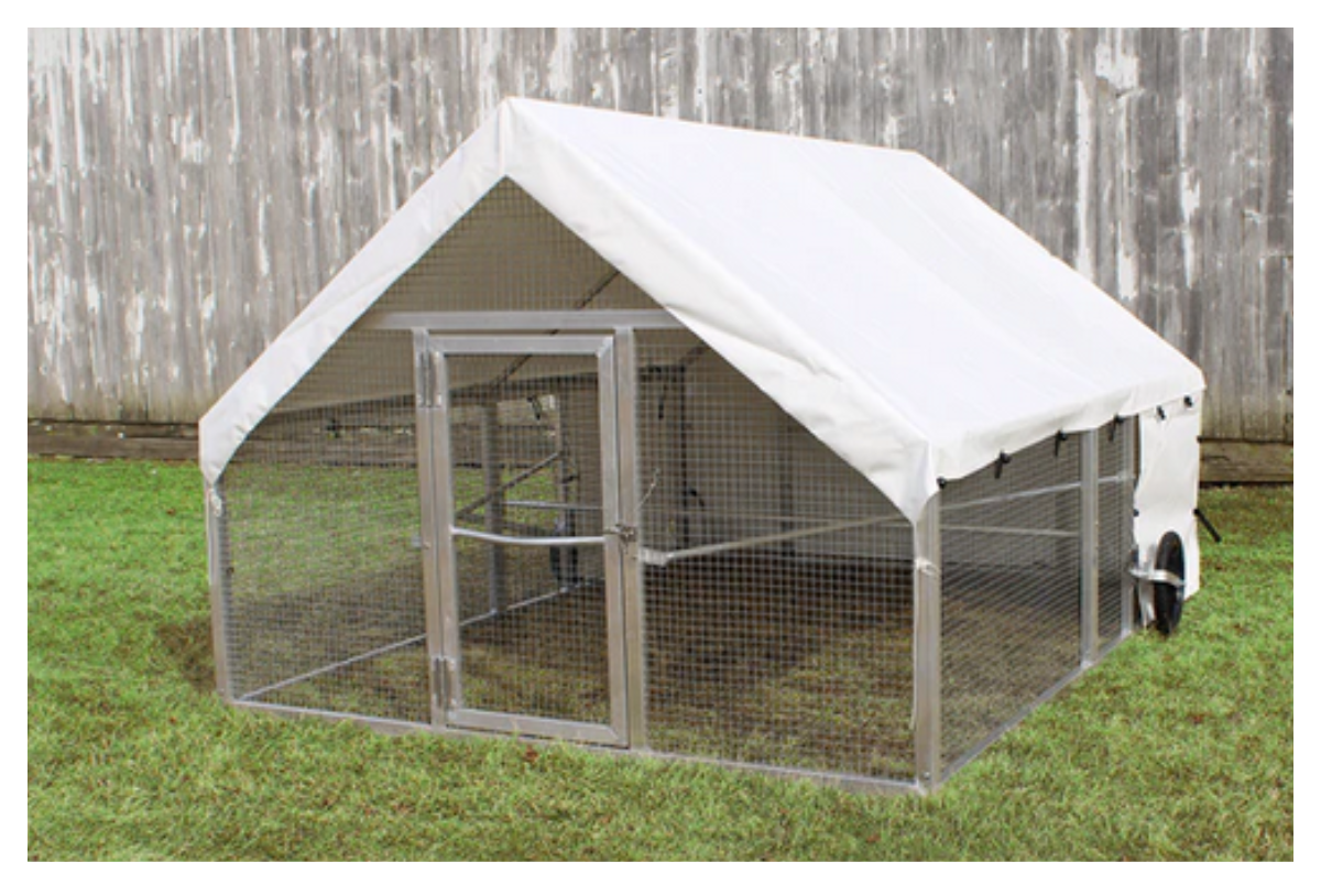 A metal animal enclosure with a white canopy cover attached to a wooden fence in a grassy yard.