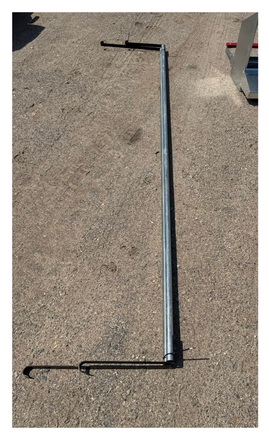 A metal frame with a long straight section and two hooks at one end, lying on a dirt surface outdoors.