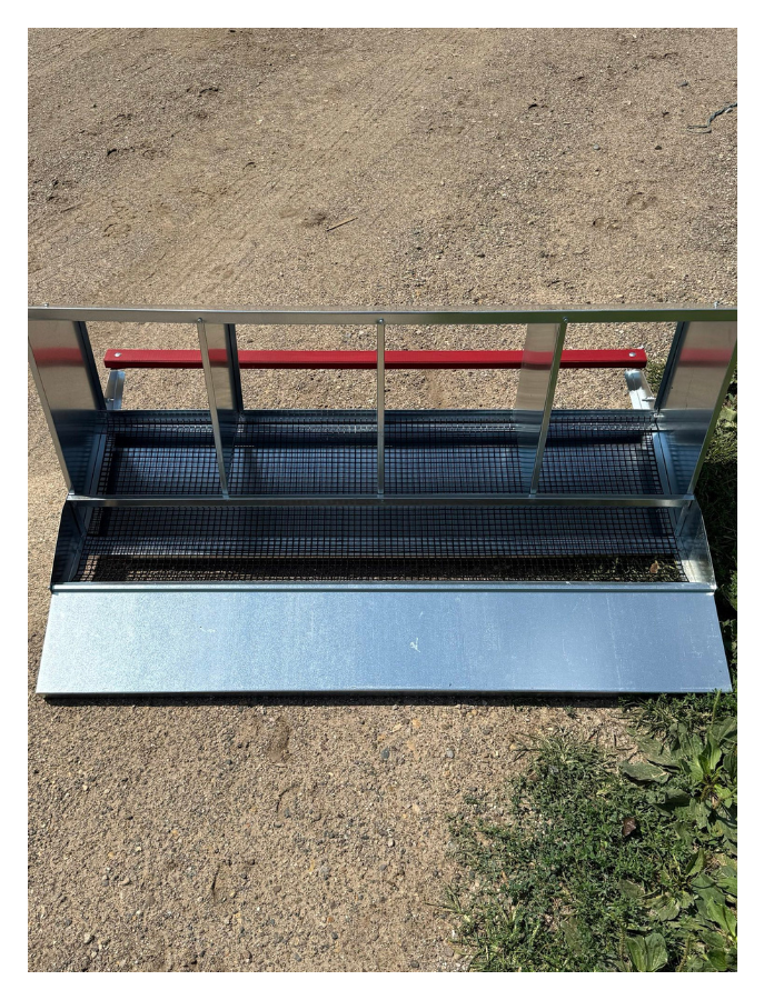 Empty retail store display shelf with a metal frame and a red horizontal bar, situated outdoors on a dirt surface.