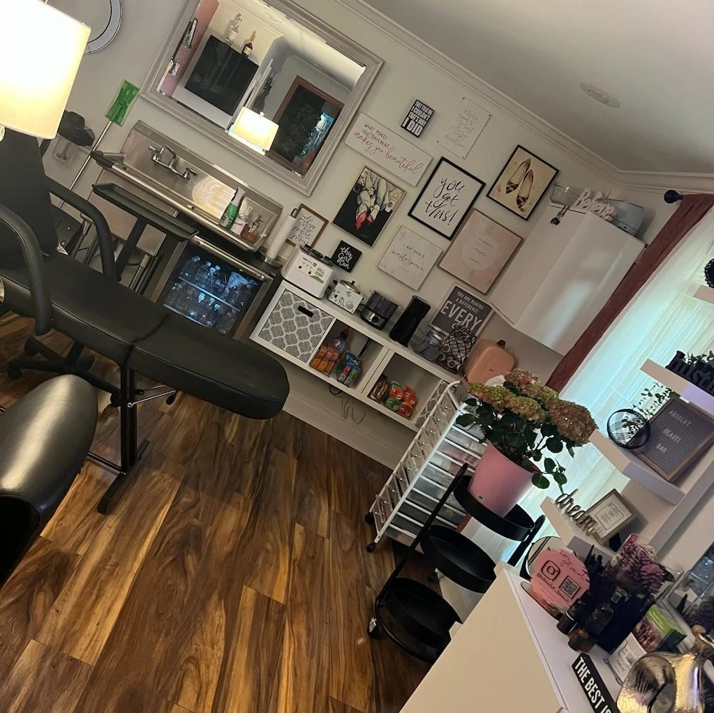 Interior of a beauty studio with a massage chair, wall art, shelves with products, a small refrigerator, a sink, and decorations.