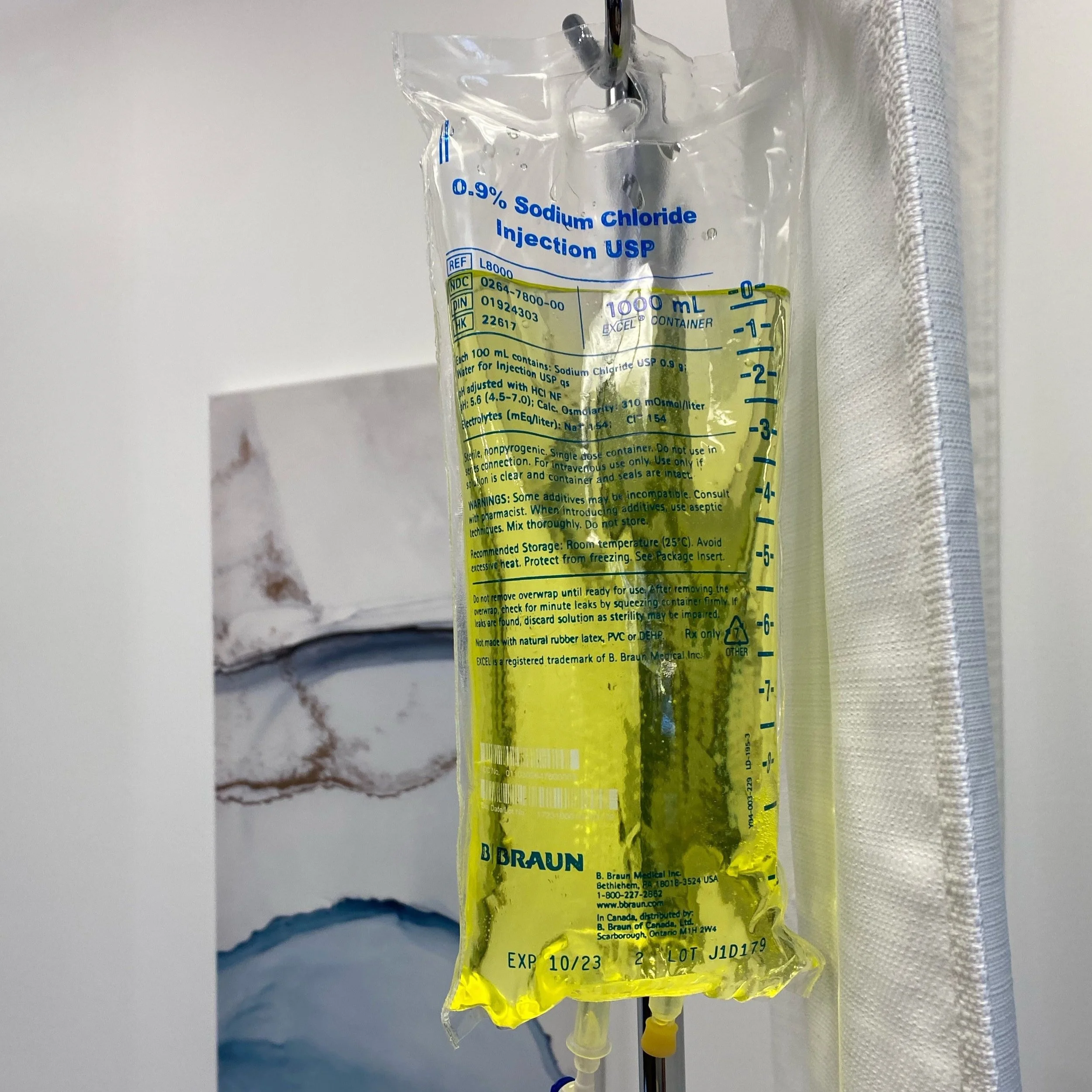 A bag of 0.9% Sodium Chloride Injection USP with yellow liquid, labeled with measurements and a brand name, hanging in a medical setting.