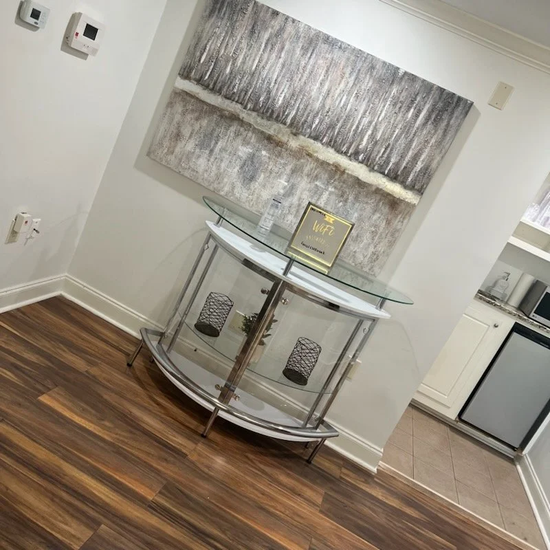 Modern hallway with a glass-topped console table, abstract artwork on the wall, and wooden flooring; a WiFi sign on the table.