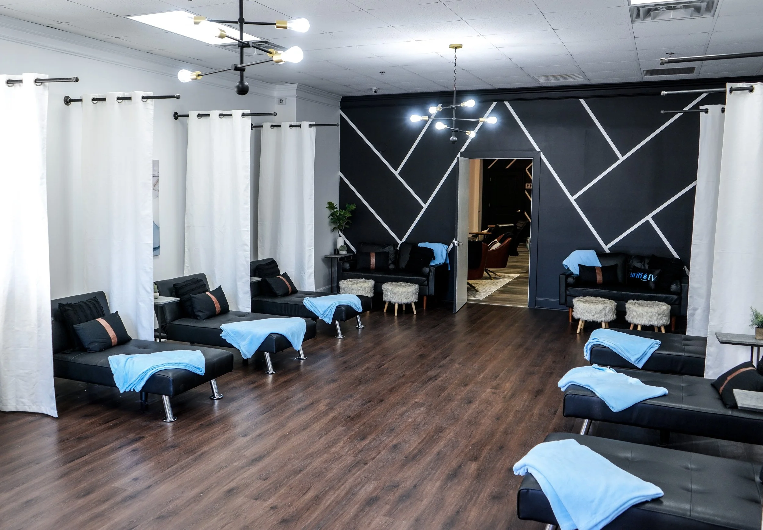 Modern lounge with black recliners, blue blankets, white curtains, and geometric wall design.