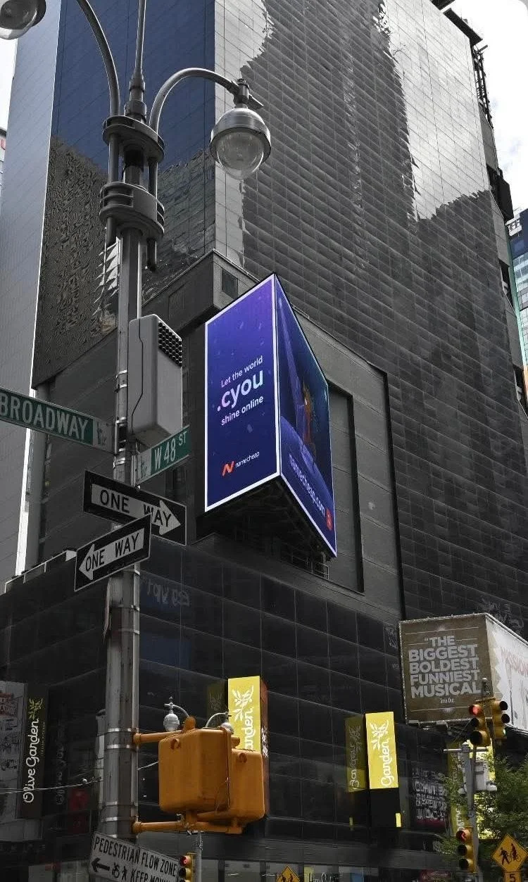 Street corner in Times Square, New York City with street signs for Broadway and W 48th Street, electronic billboard advertising Verizon, traffic lights, and a building with reflective dark glass exterior.
