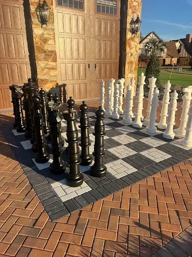 Large outdoor life-size chess game with black and white pieces on a tiled chessboard paver installation. Entertaining patio design in Viera, FL