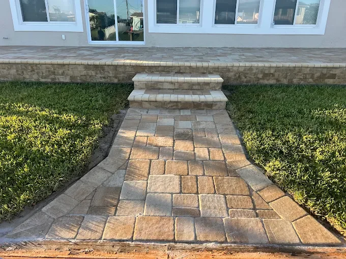 Stone walkway with steps leading up to a house door, flanked by green grass.