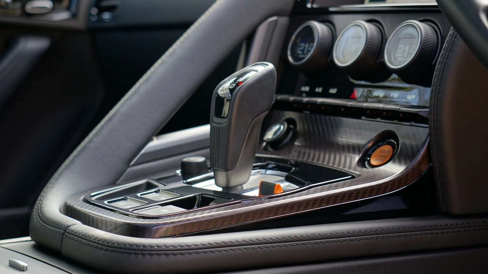 Close-up of a luxury car interior center console with gear shift, climate controls, and start button.