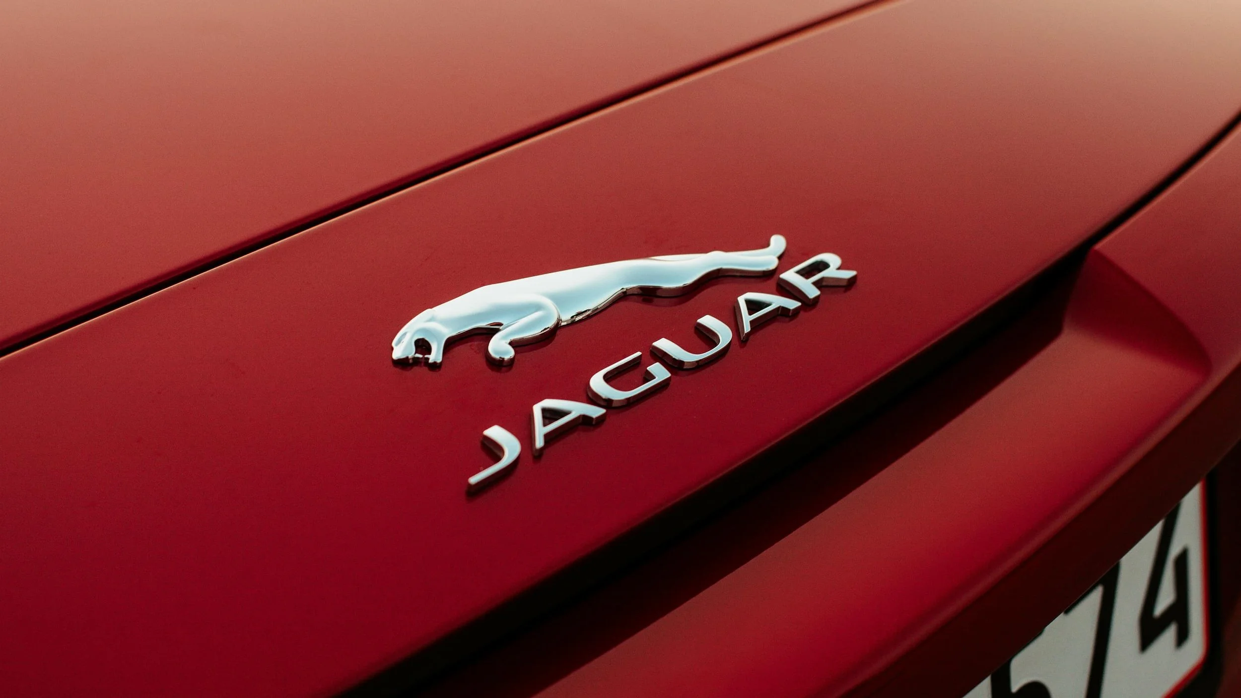 Close-up of a red Jaguar car hood with a silver jaguar emblem and the word 'JAGUAR' on it.