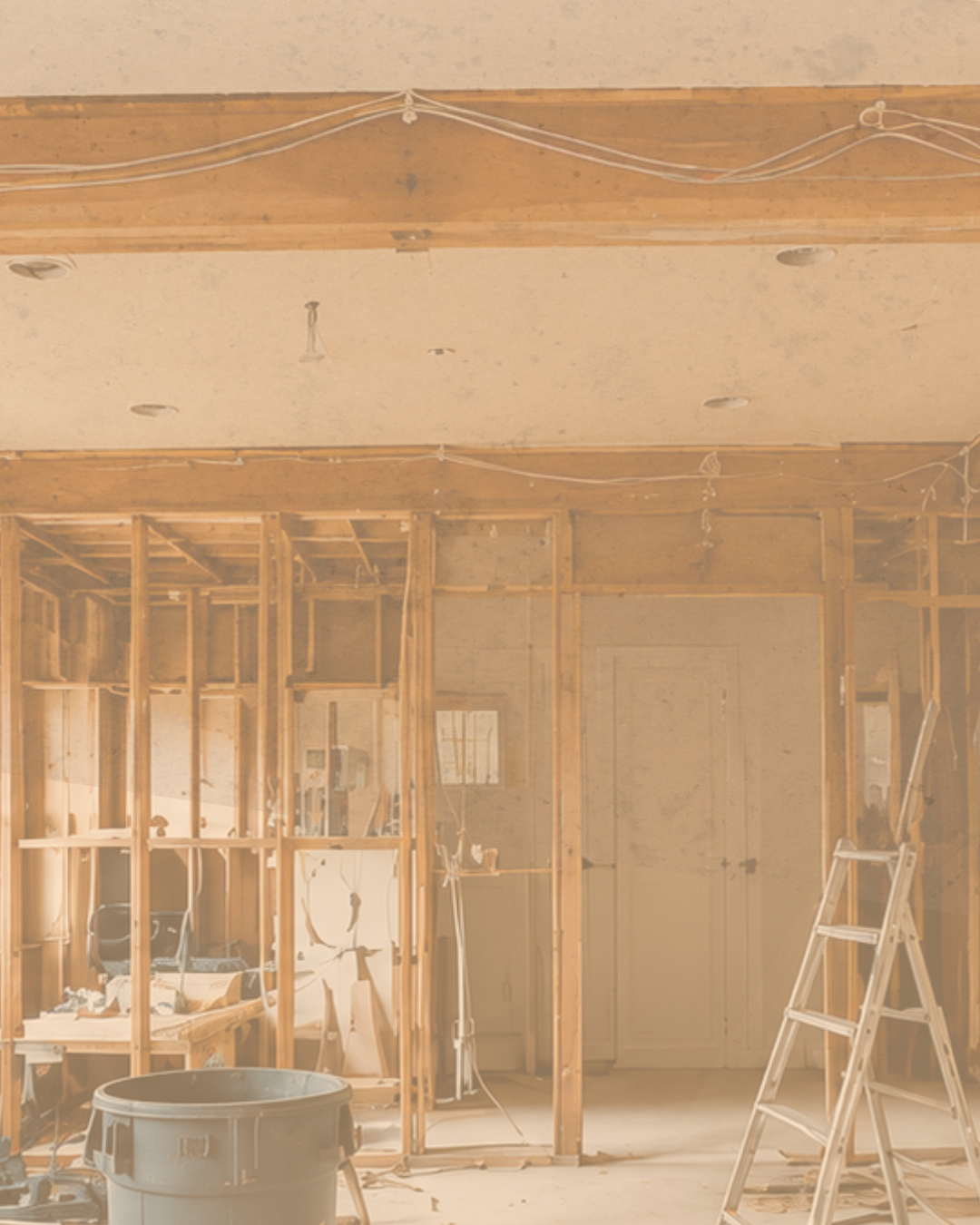 Interior of a house under renovation, with exposed wooden studs, a ladder, construction tools, and scattered materials.