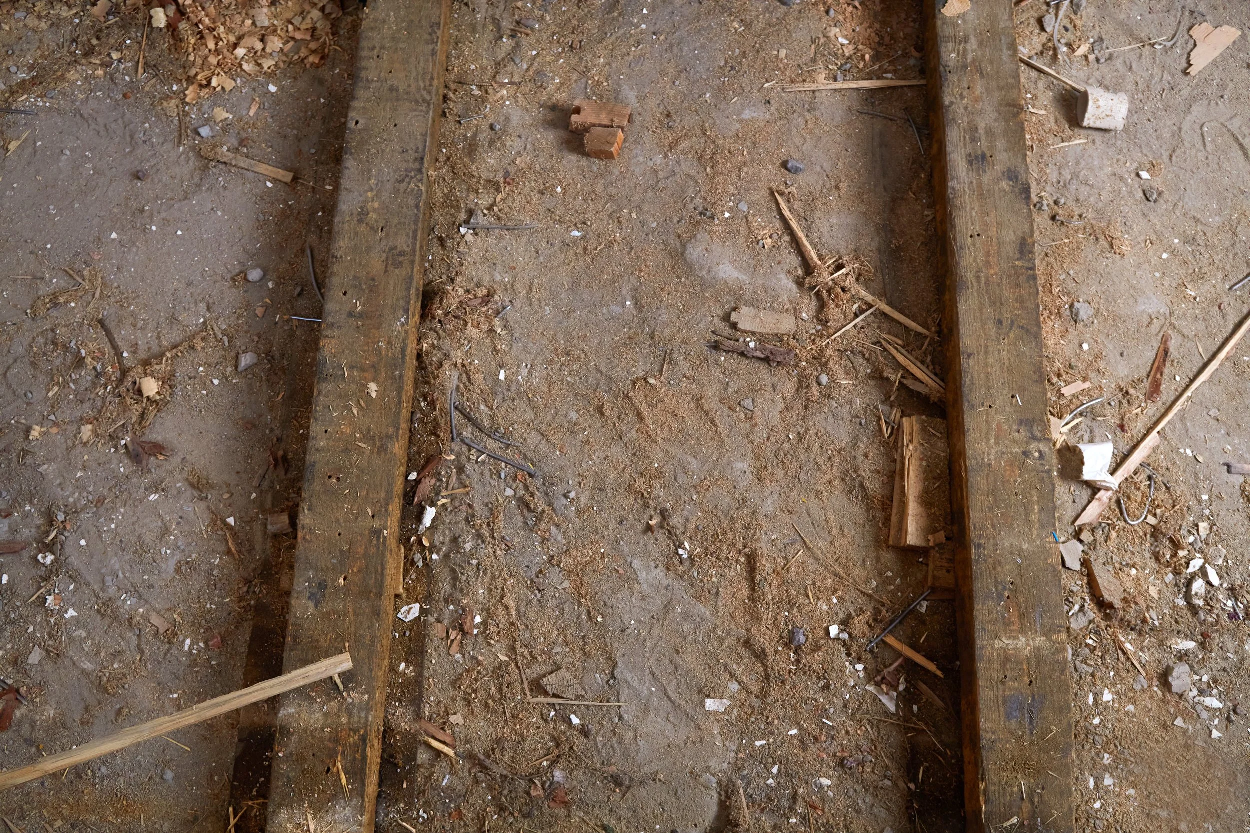 A dirt floor with scattered wood debris and two parallel wooden beams, with small bricks near the center.