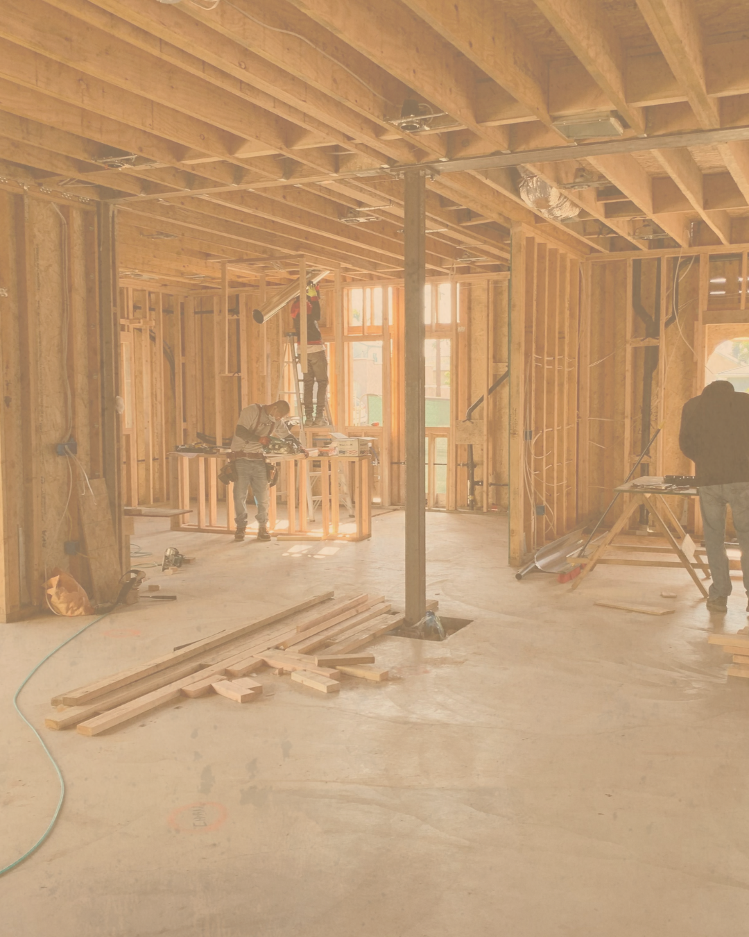 Construction workers building the wooden framework of a house inside. Luminous light coming through large windows.
