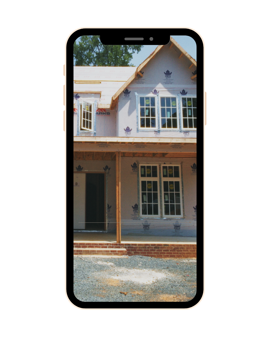 A house under construction with framing and windows installed, viewed through a phone screen.