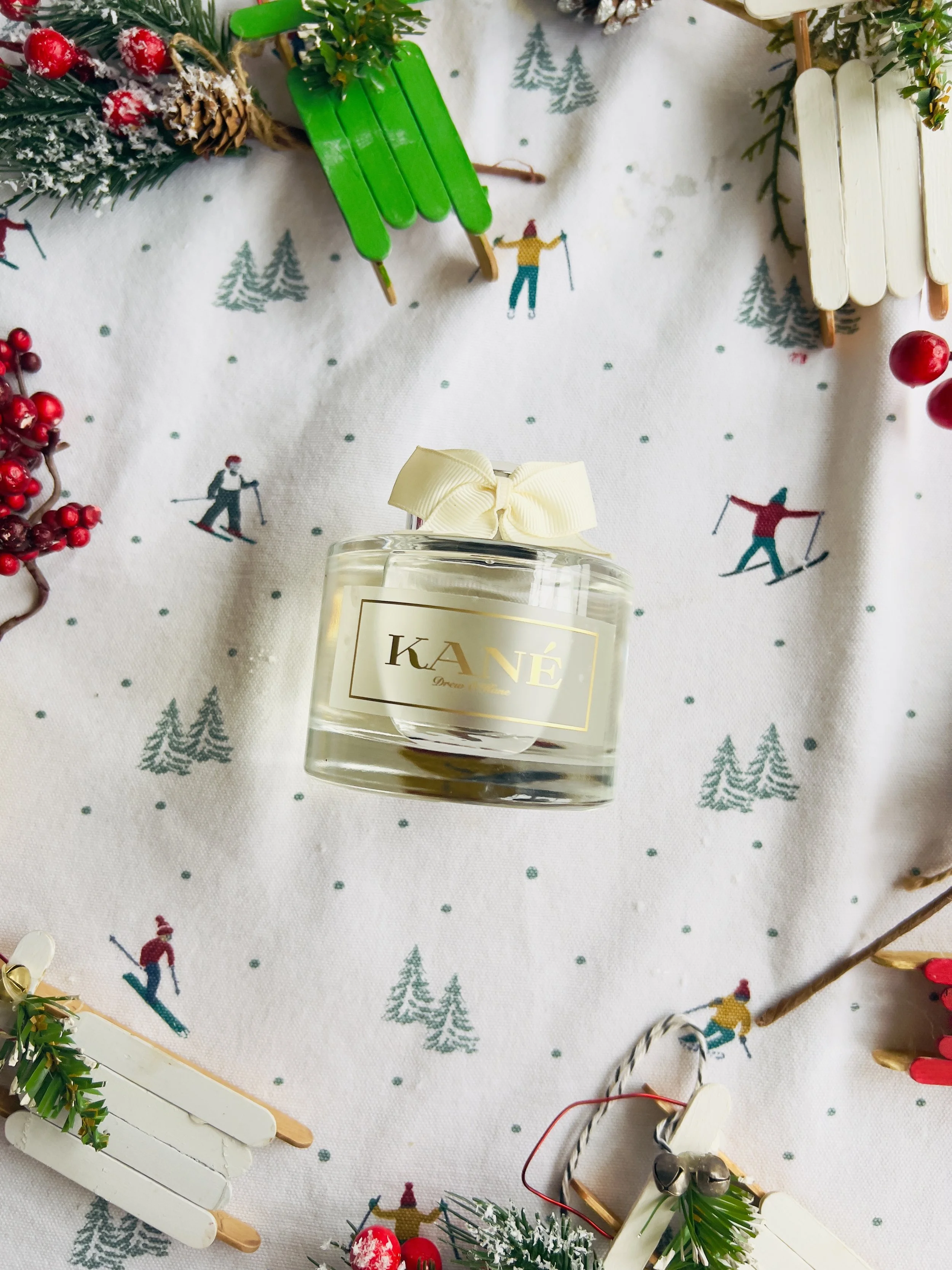Decorative setting with a candle, Christmas pinecones, and miniature sleds on a tablecloth with skier and winter scene patterns.