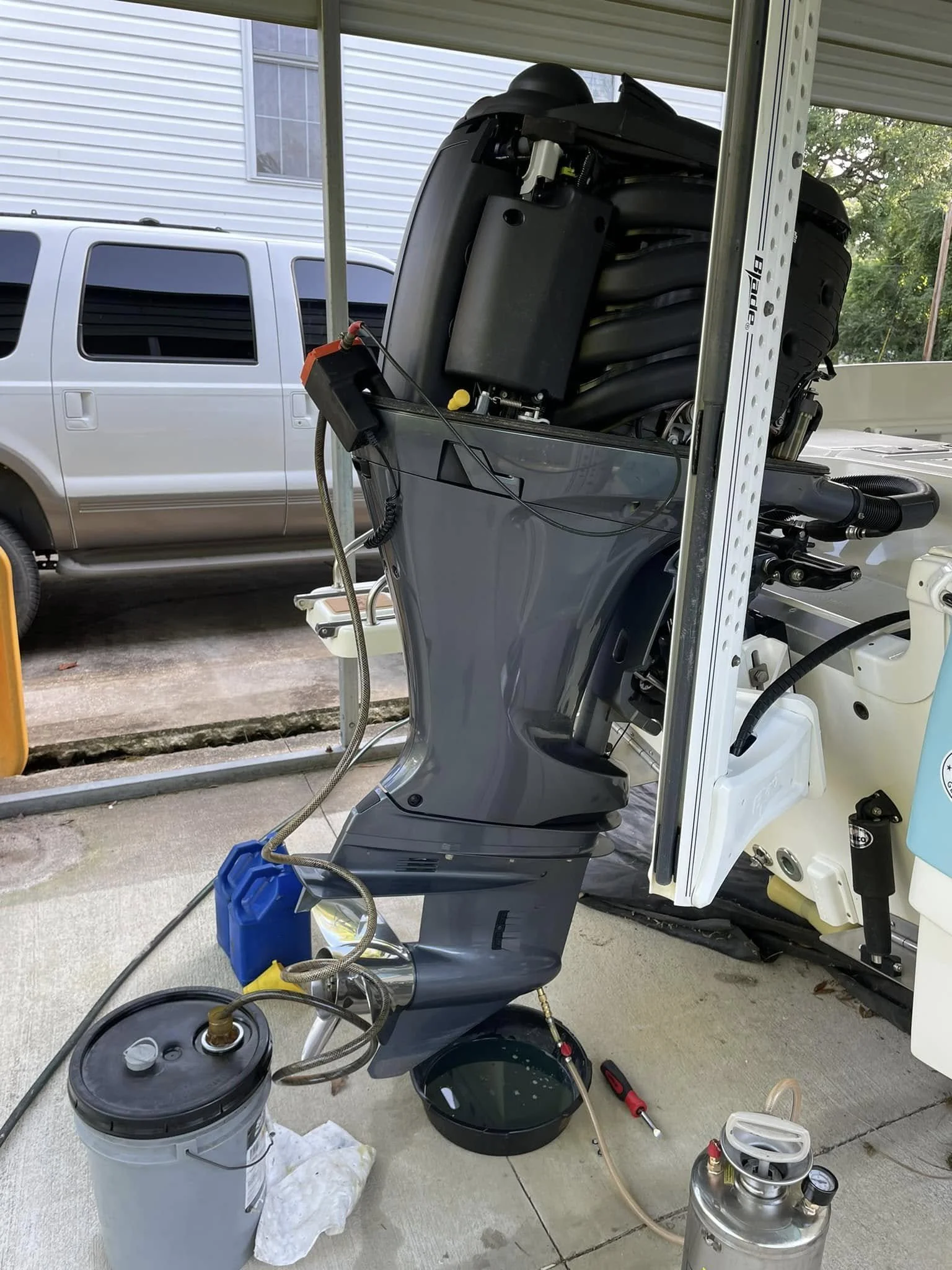 Outboard motor being serviced or repaired on a garage floor with tools and containers nearby, parked outside a house.