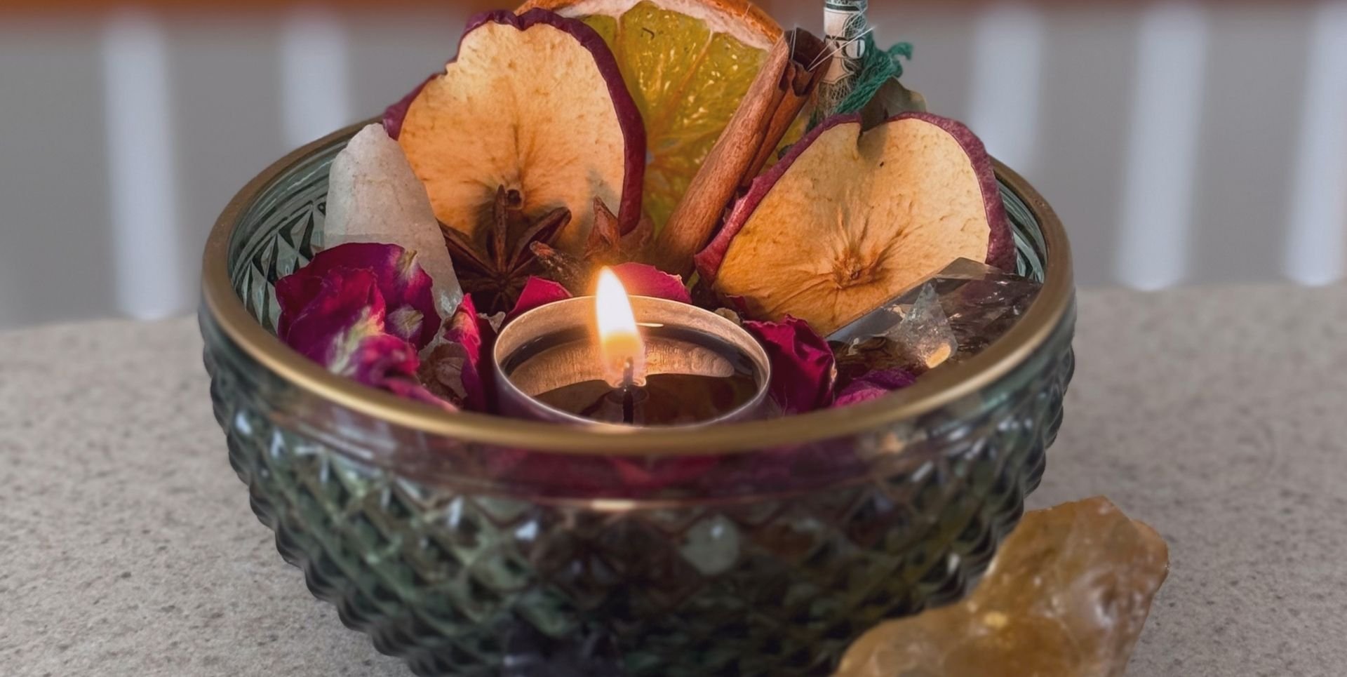 a green glass bowl filled with fuchsia flowers, dried apple slices, crystals, and a tea light candle