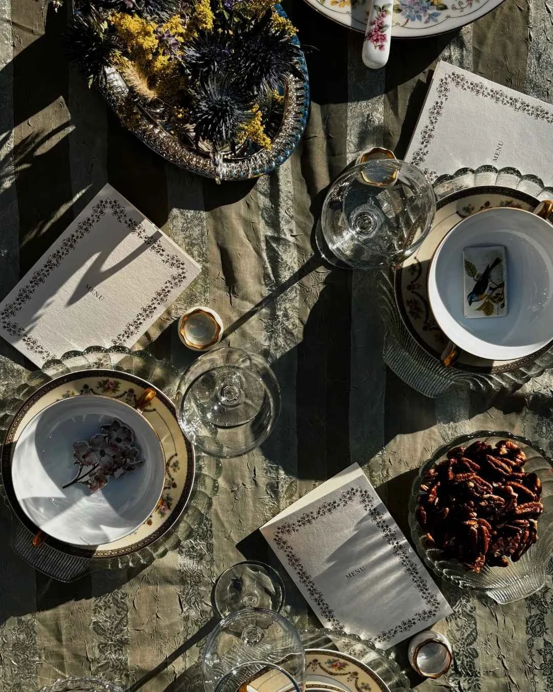 overhead view of a table set with teacups, dishes filled with herbs, notecards, and empty wine glasses