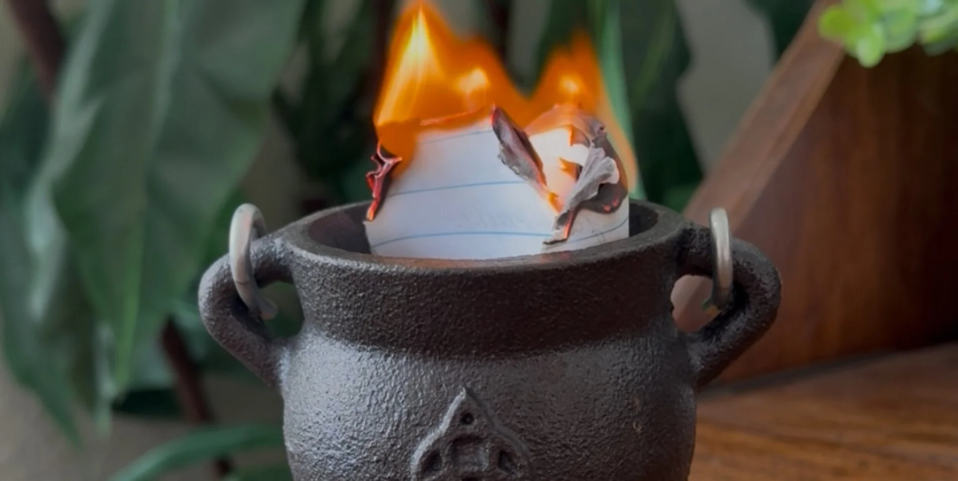 a folded piece of notebook paper burning in a small cauldron on a desk