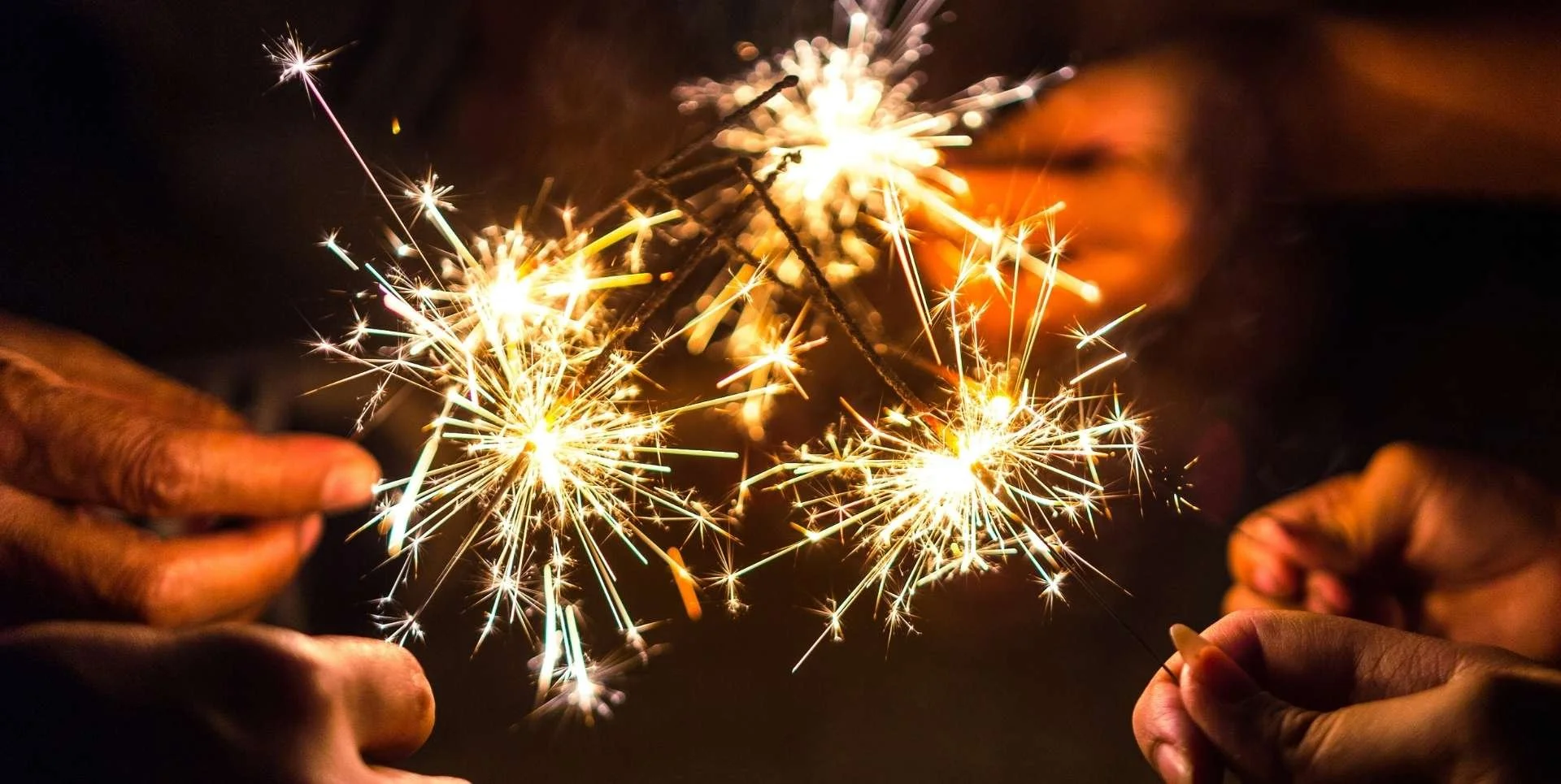 several hands showing lit sparklers held close together