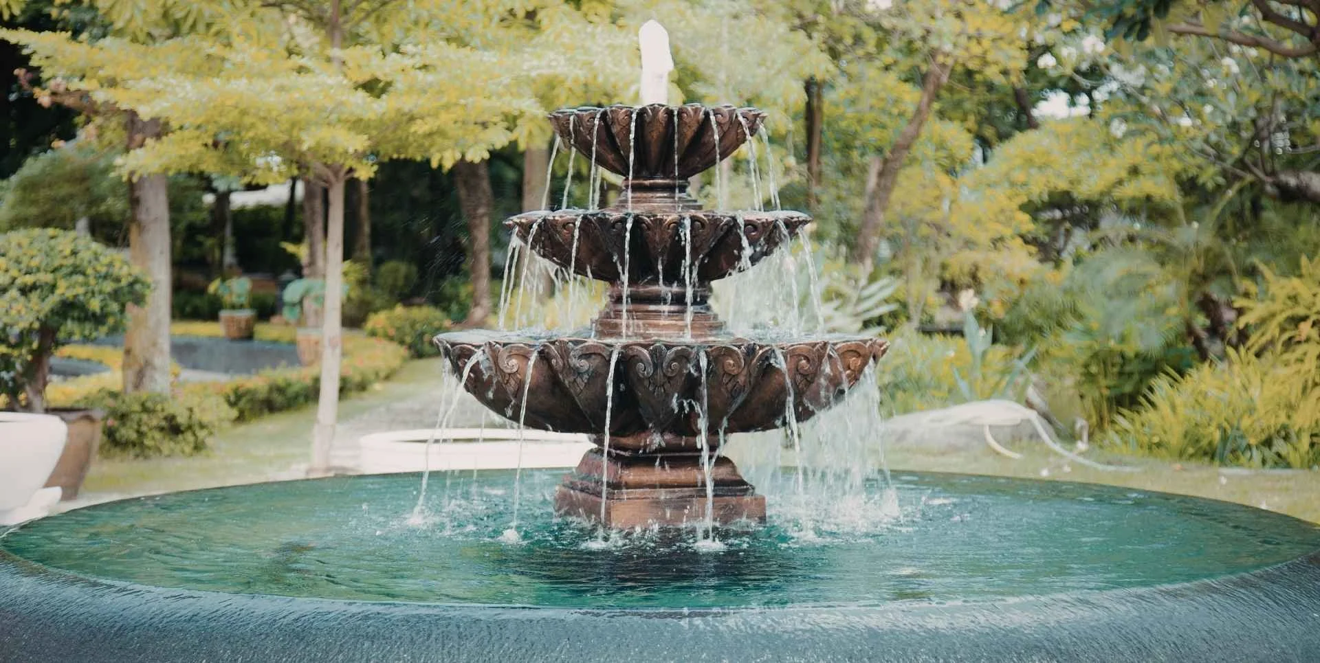 an ornate fountain with turquoise water, surrounded by lush greenery