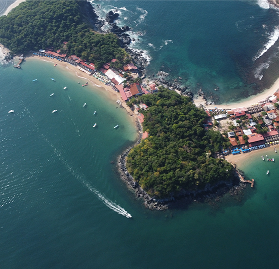 Aerial view of a coastal area with a small island, beaches, boats, and surrounding buildings and greenery.