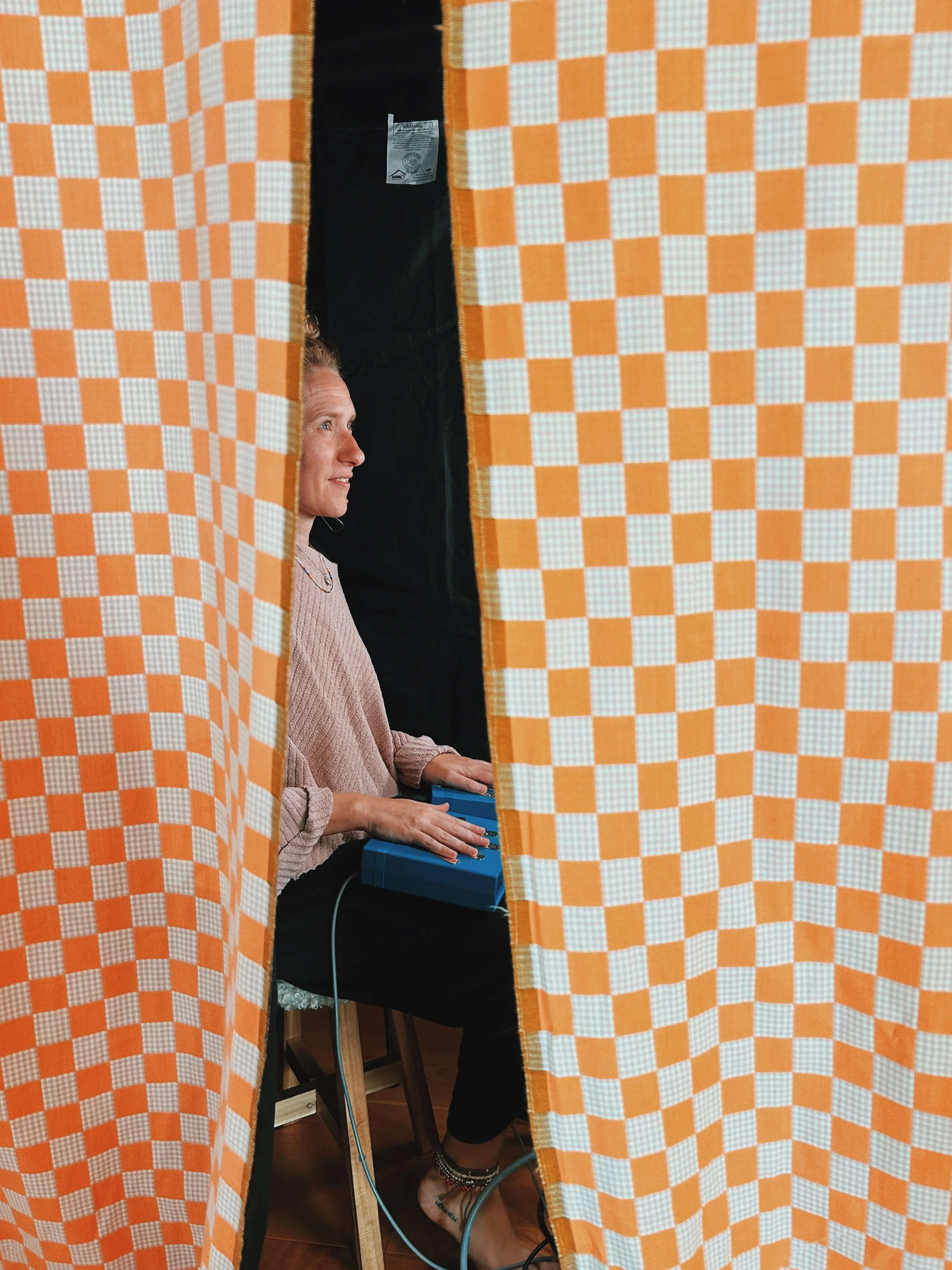 Woman playing a blue electronic keyboard, seen through a gap in orange checkered curtains.