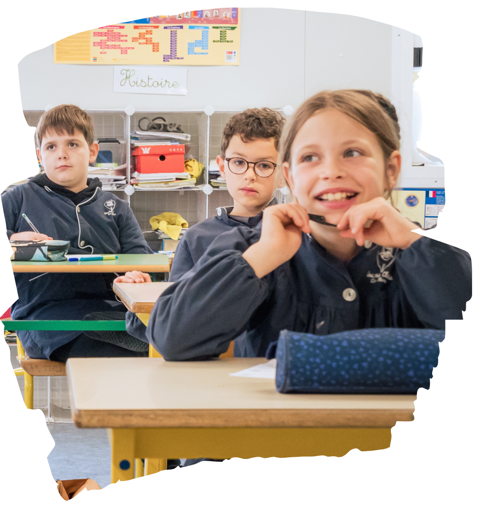 Trois enfants dans une classe, assis à leur bureau, avec une affiche sur le mur derrière eux