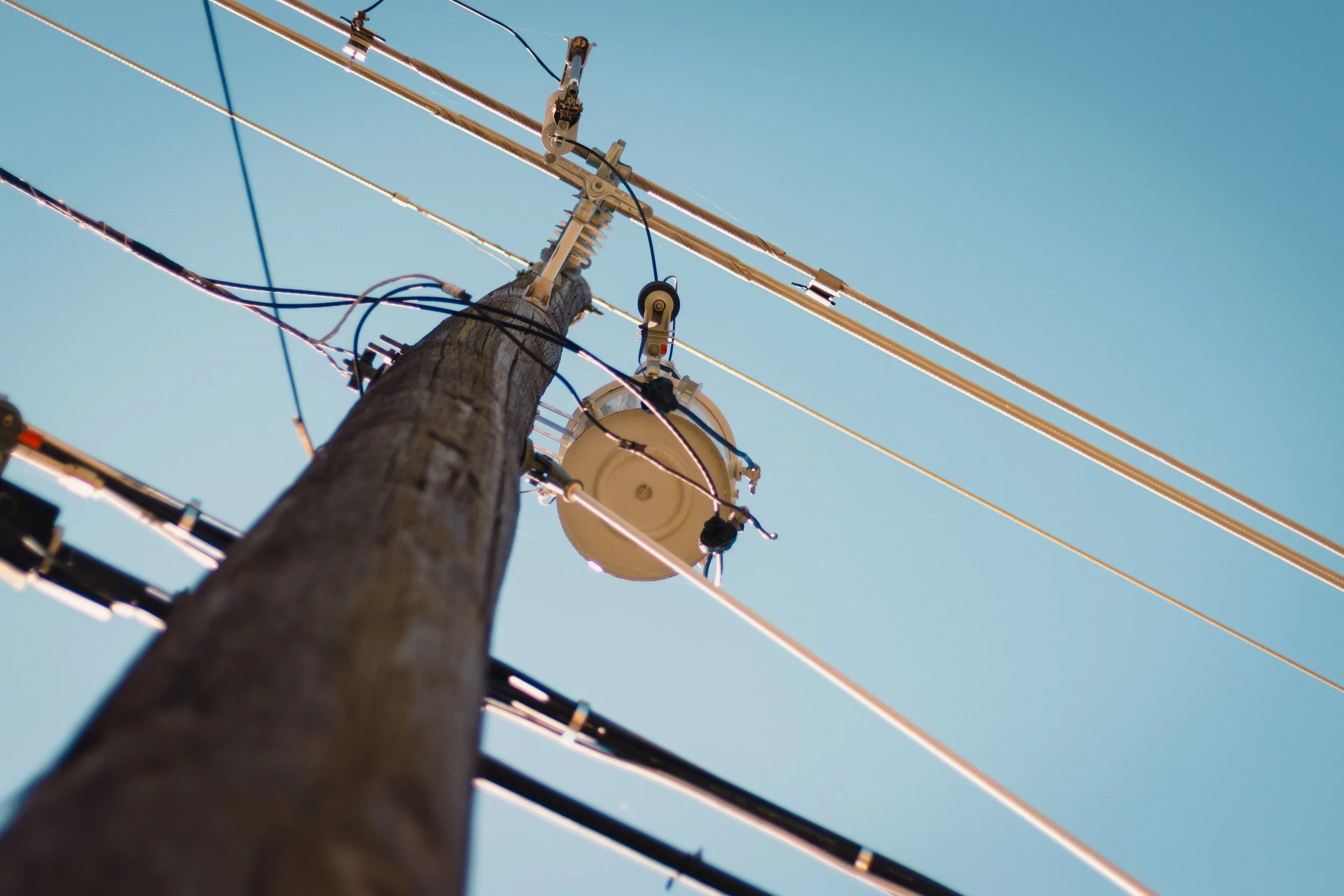 Low-angle view of an electrical utility pole with insulators and power lines against a clear blue sky.
