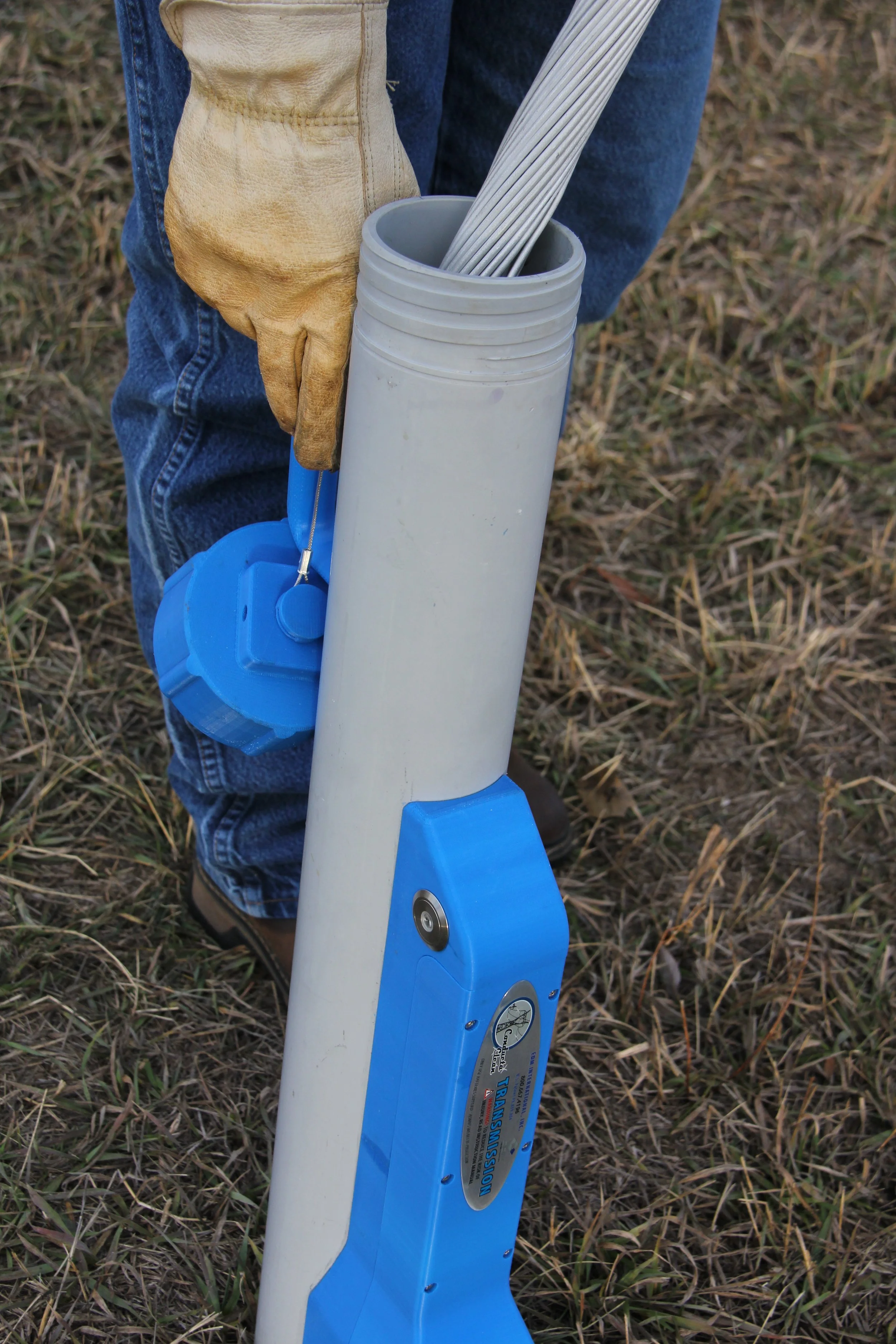 Person holding a blue and white pipe launcher with an electronic timer attached, on a grassy field.