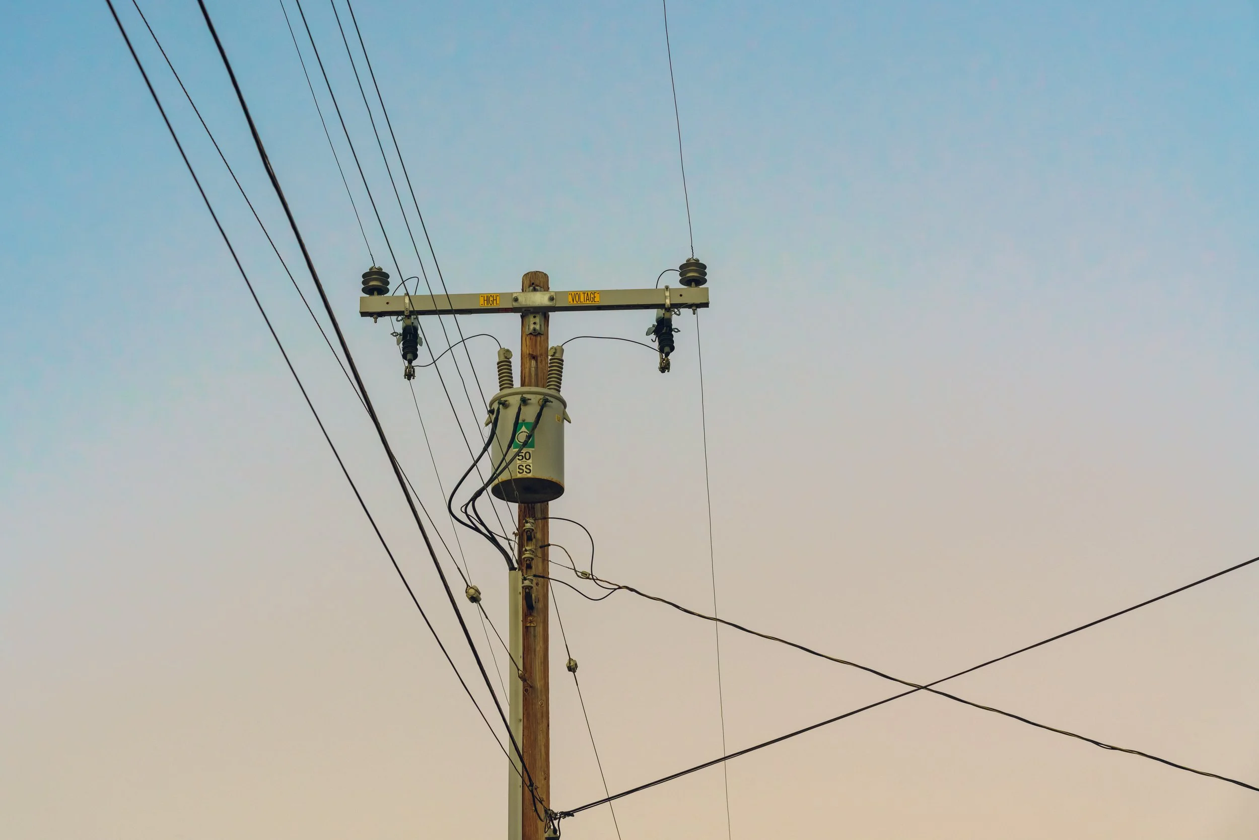 A wooden utility pole with multiple electrical wires and insulators against a clear sky.