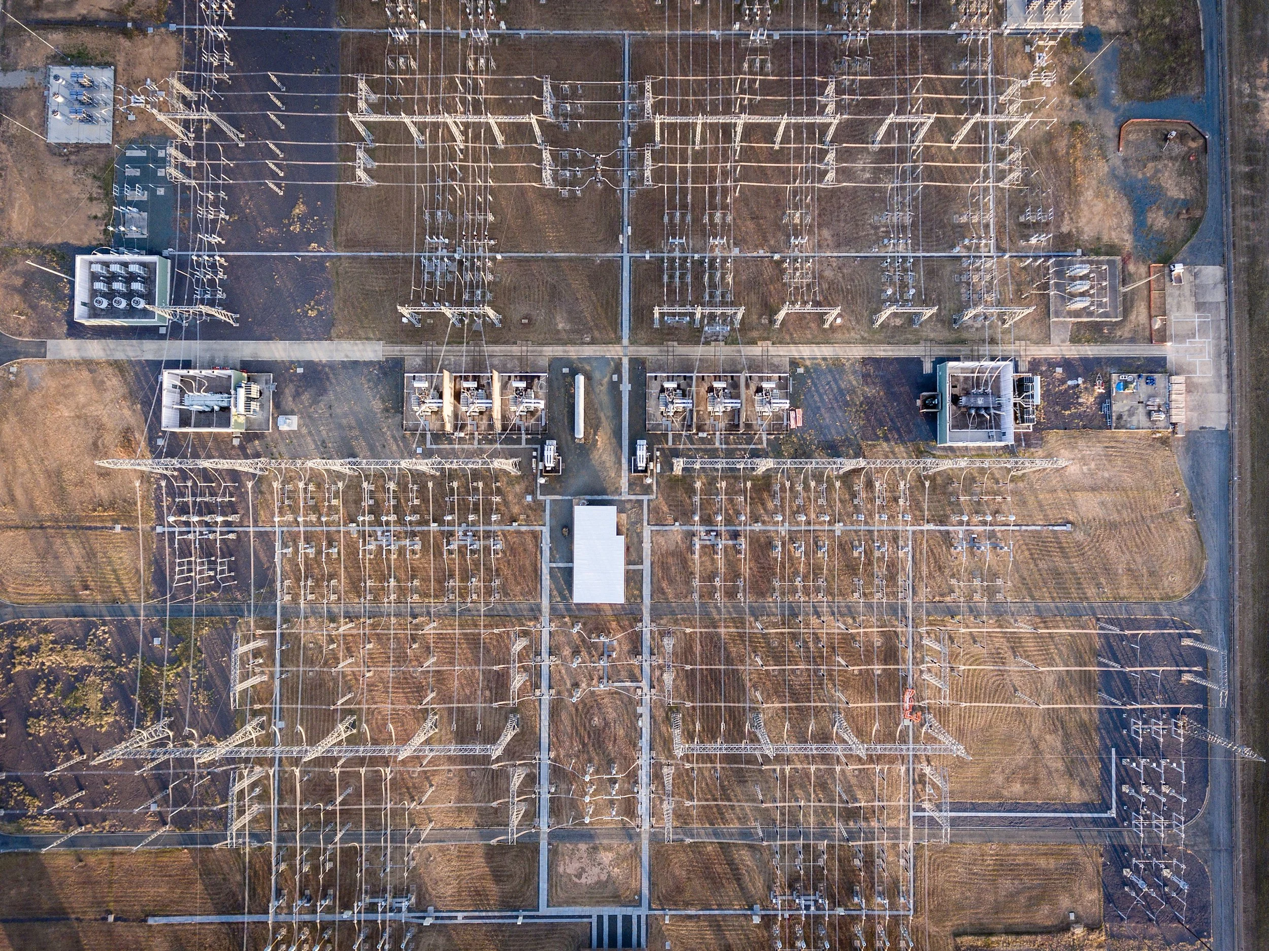 An aerial view of an electrical substation with multiple transformers, power lines, and equipment organized within a fenced perimeter.