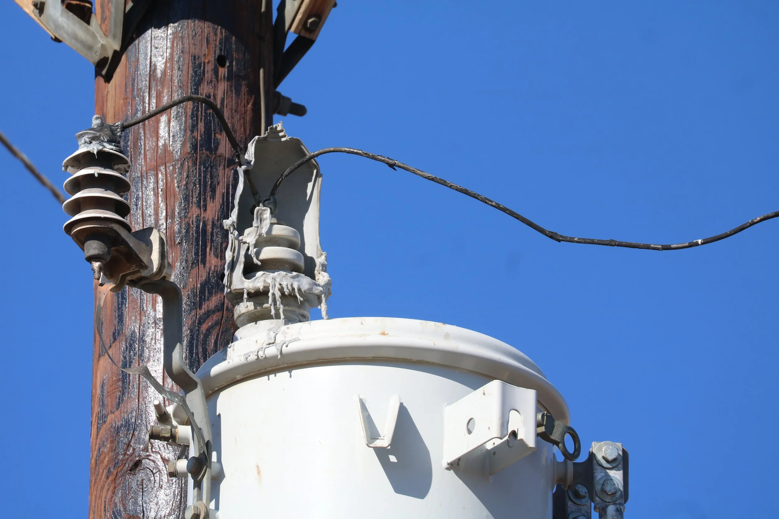 Close-up of electrical power pole with transformers, insulators, and wires against a clear blue sky.