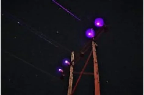 Power line pole with purple-lit insulators against a night sky with visible stars.