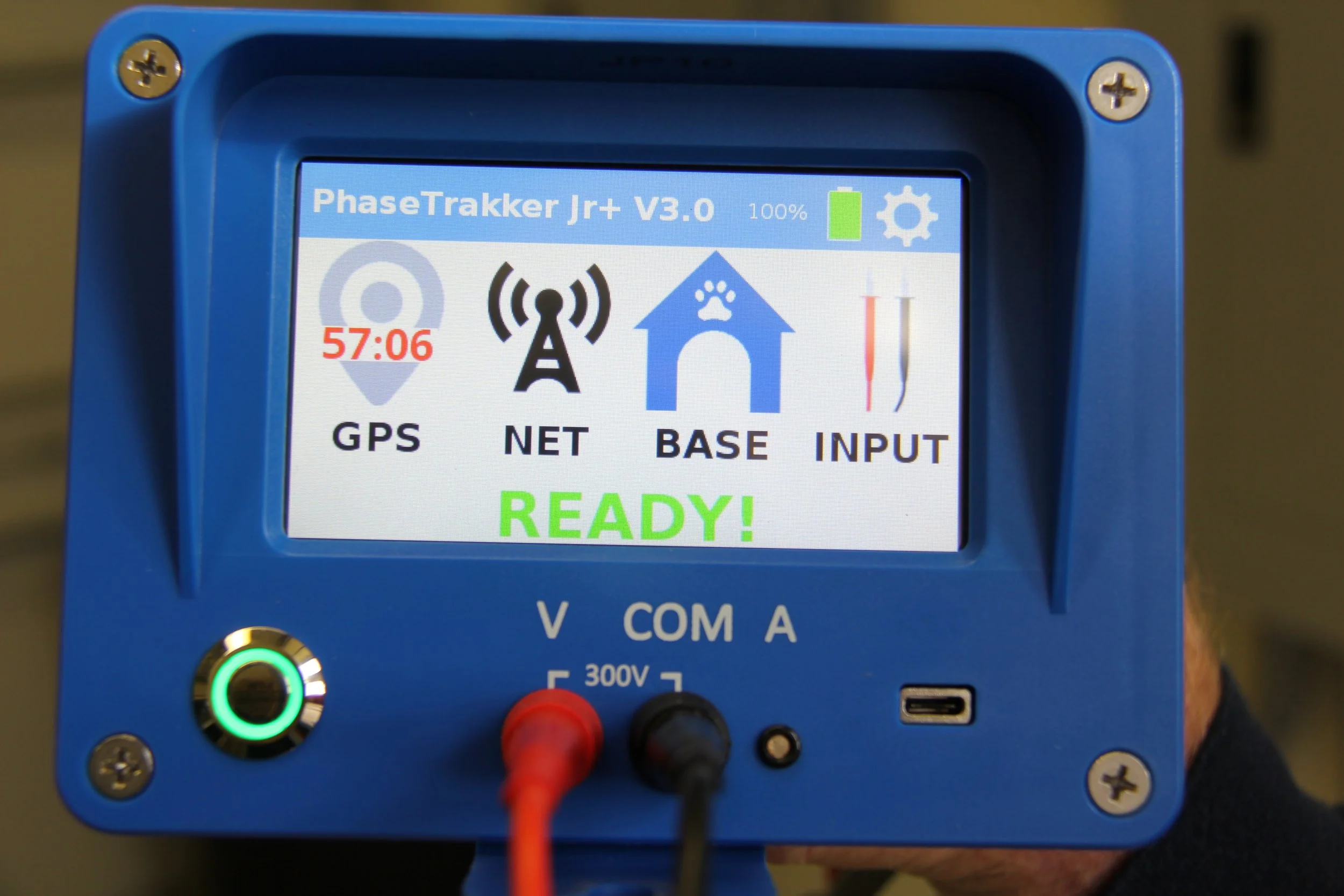 Digital device screen displaying status for PhaseTrakker Jr+ V3.0, showing GPS, NET, BASE, and INPUT indicators, with a green 'READY!' message, and red and black alligator clips connected at the bottom.